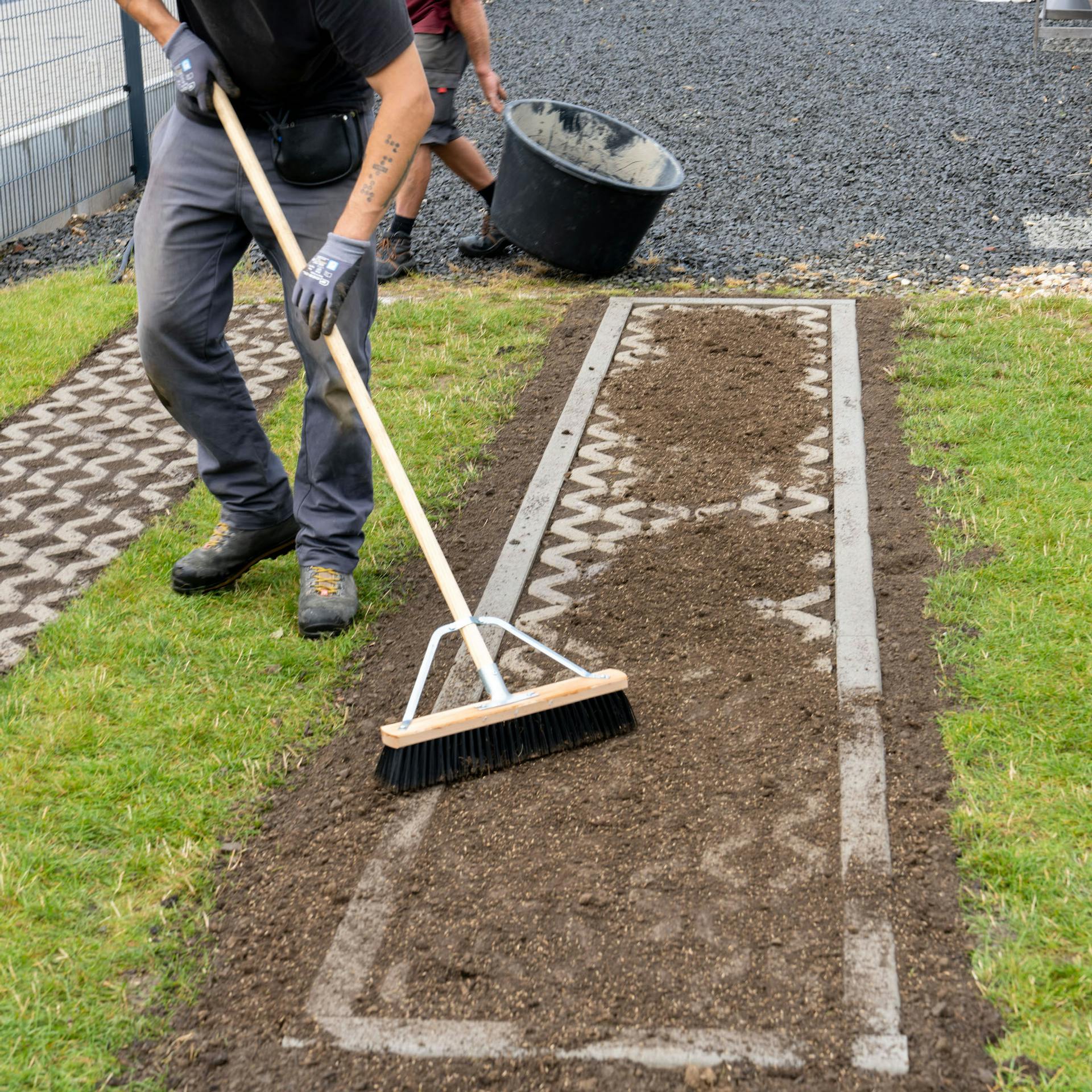 Muž zametá zeminu medzi zatrávňovacie tvárnice