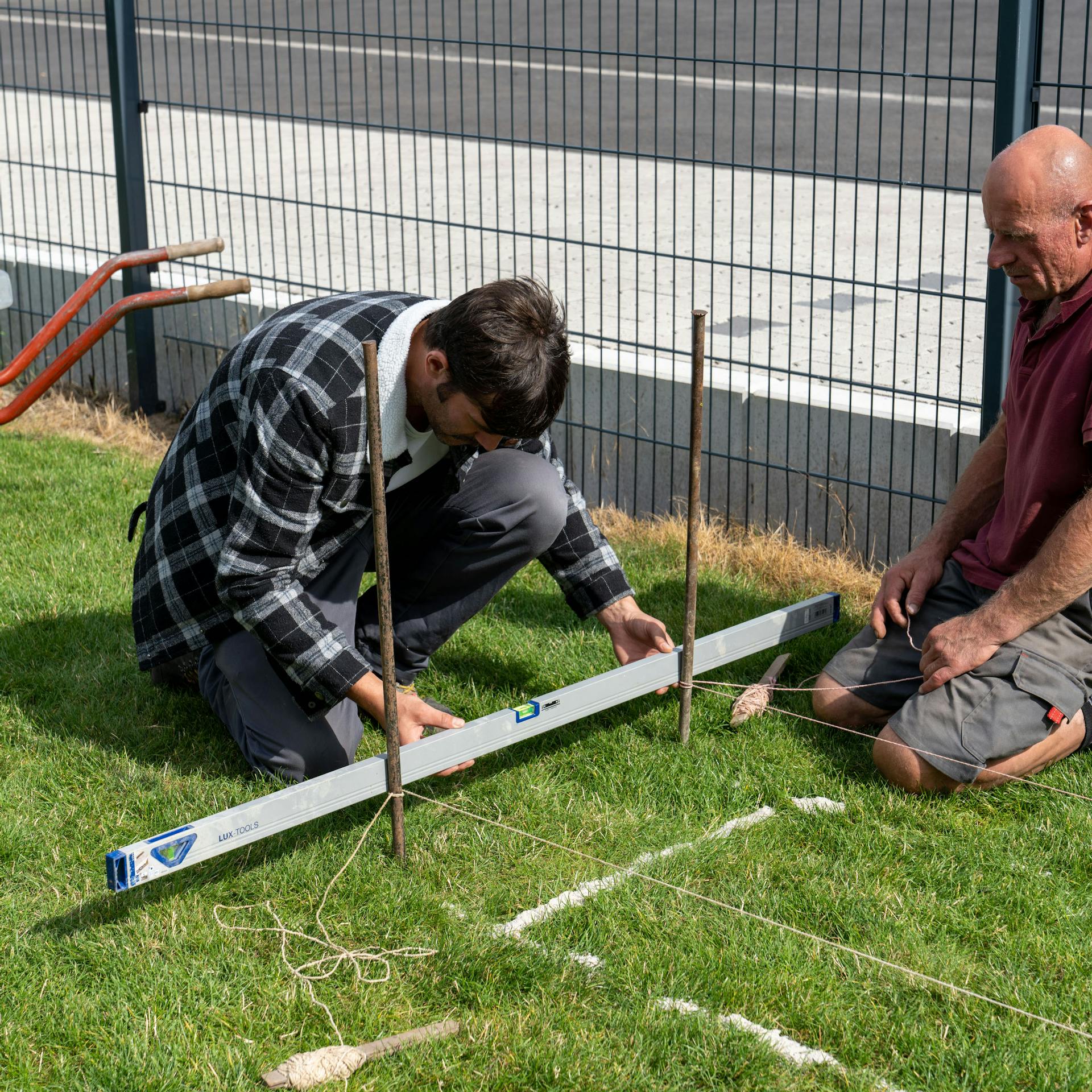 Muž drží vodováhu pri dvoch vytyčovacích kolíkoch