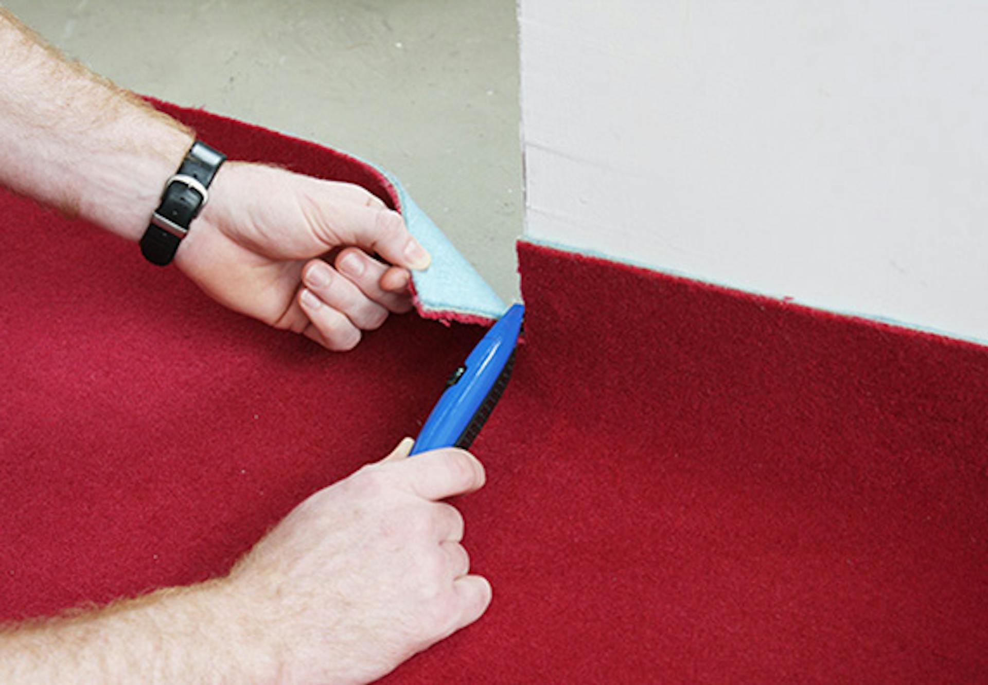 Pracovník orezáva vonkajšie rohy červeného koberca orezávacím nožom.