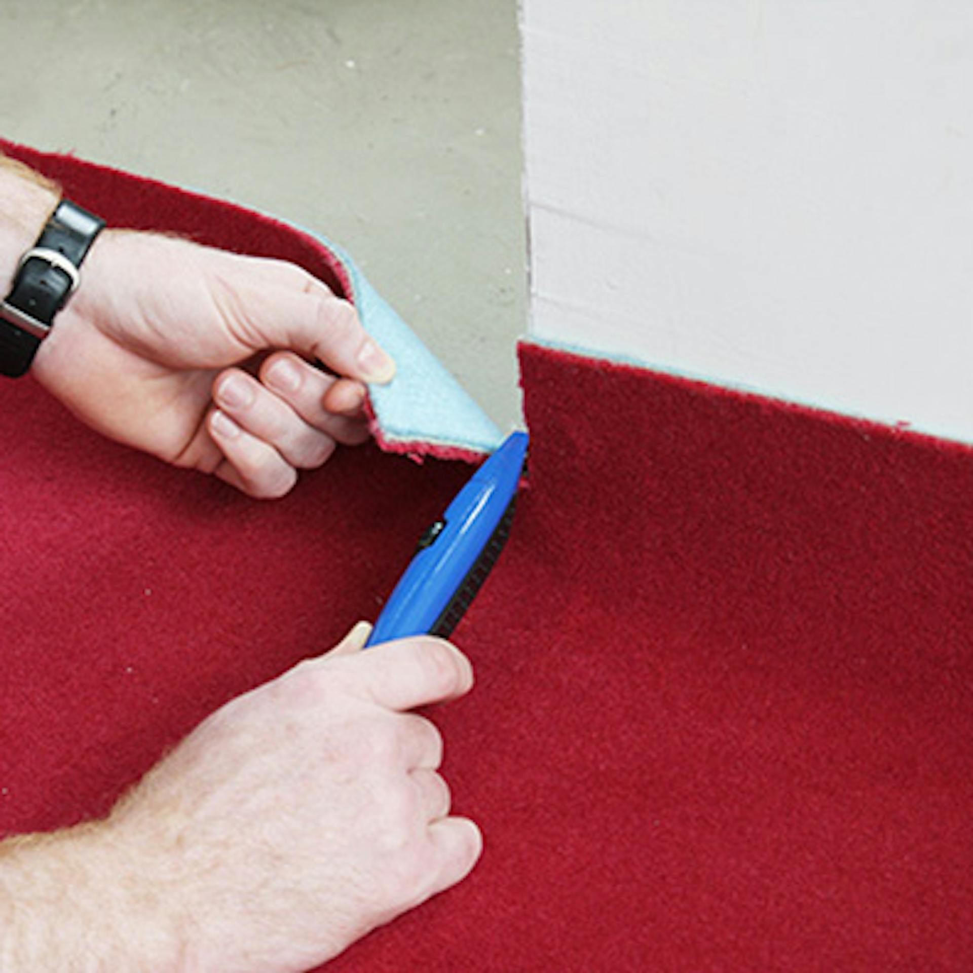Heimwerker schneidet Außenecken von rotem Teppich mit Cuttermesser zu.