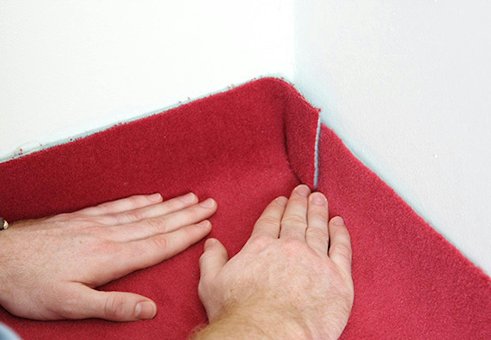 Pracovník ručne upravuje koberec v rohoch do konečného tvaru.