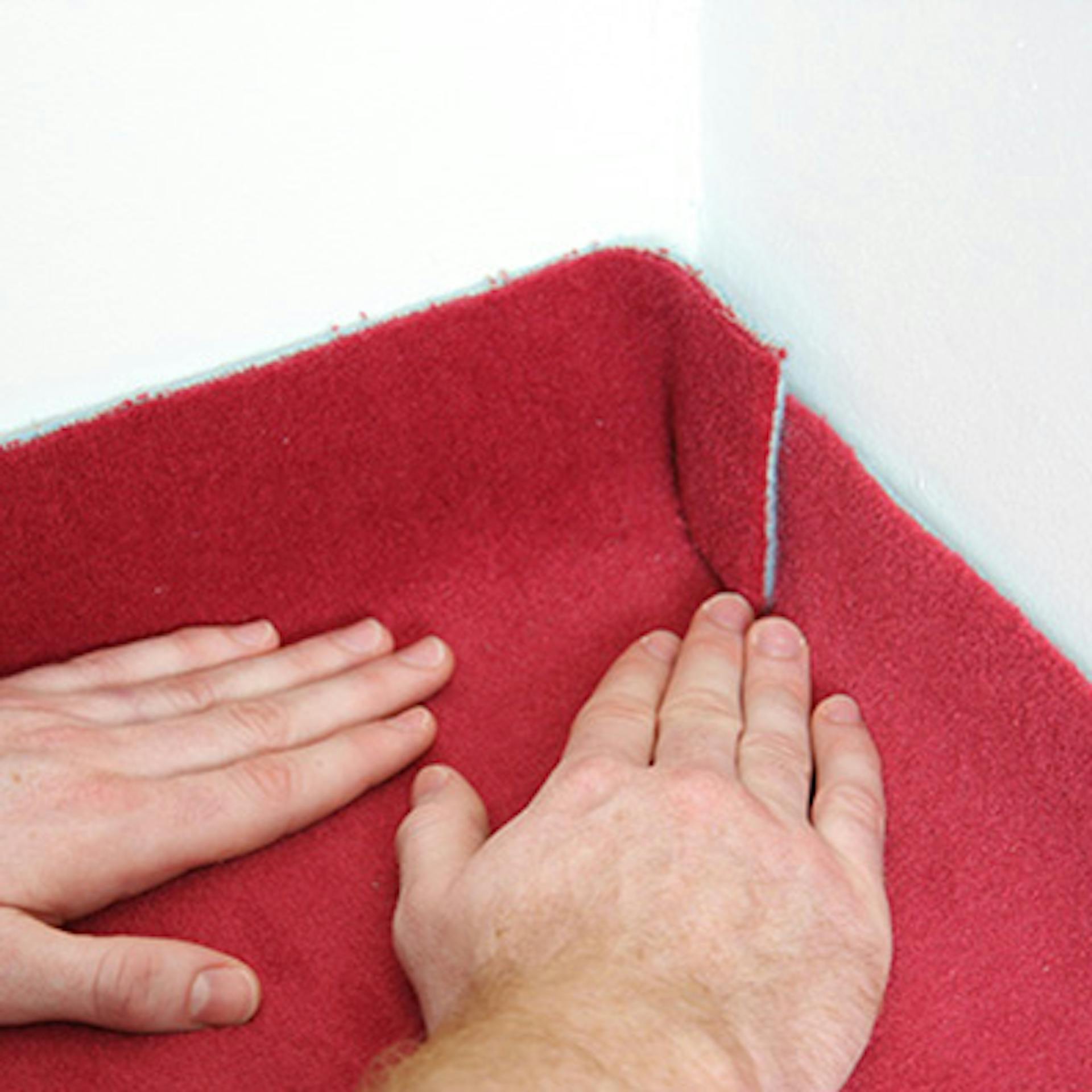 Heimwerker passt Teppichboden in den Ecken mit den Händen final an.