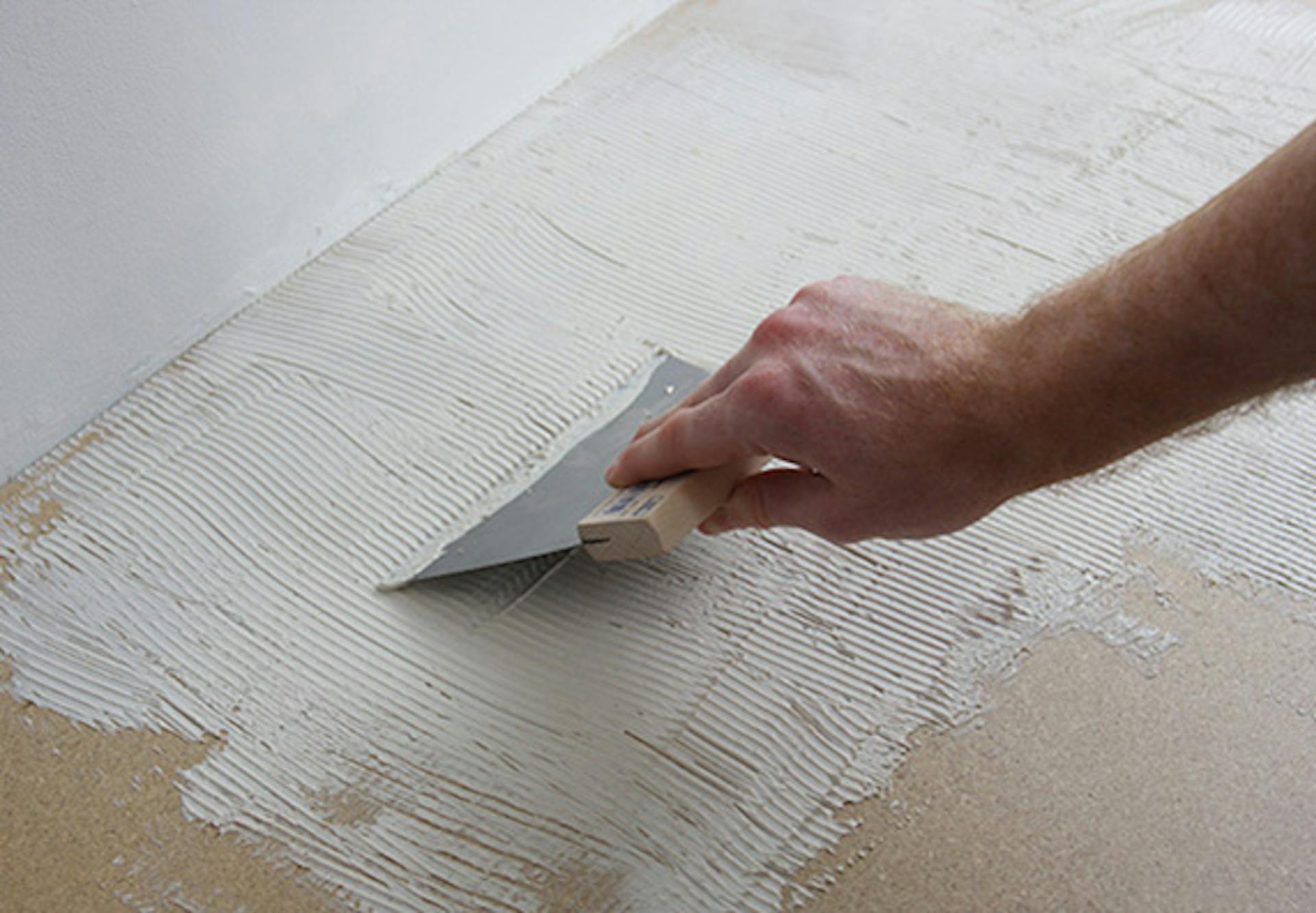 Pracovník nanáša na podklad zúbkovanou špachtľou lepidlo, aby uložil koberec.