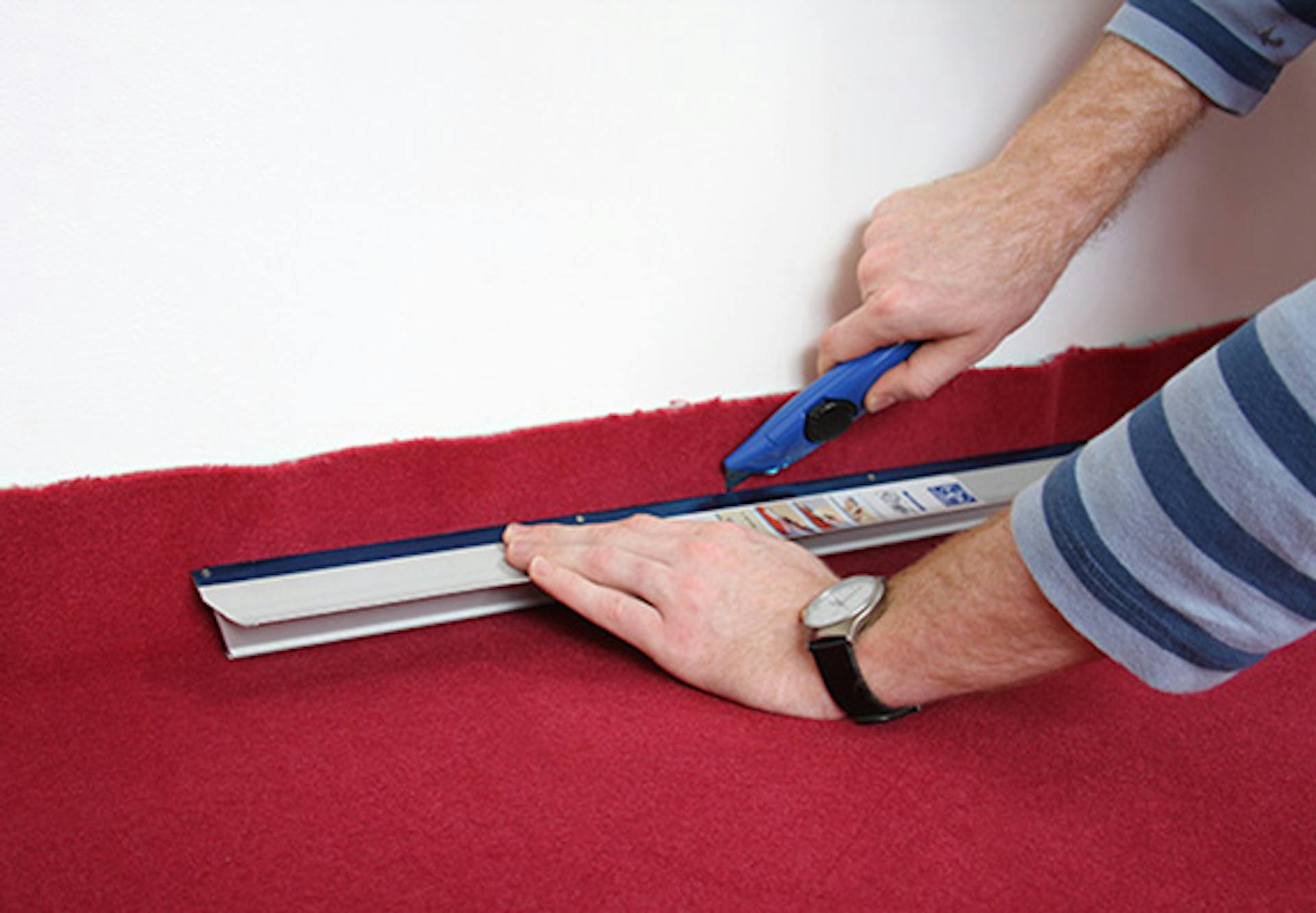 Pracovník nahrubo orezáva koberec pomocou orezávacieho noža a pravítka na rozmery miestnosti.