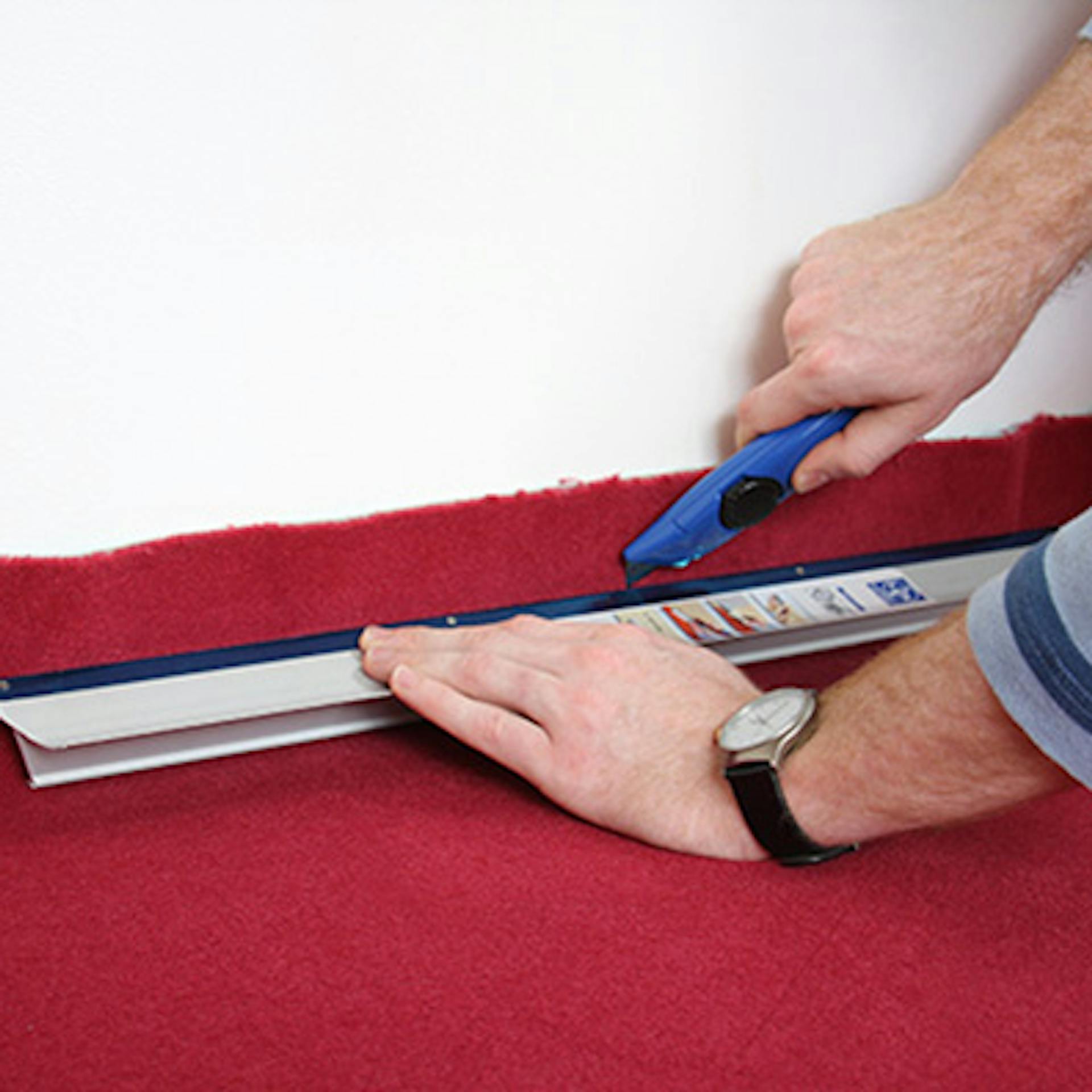 Heimwerker schneidet Teppich mit Cuttermesser und Lineal grob für Raummaße zu.