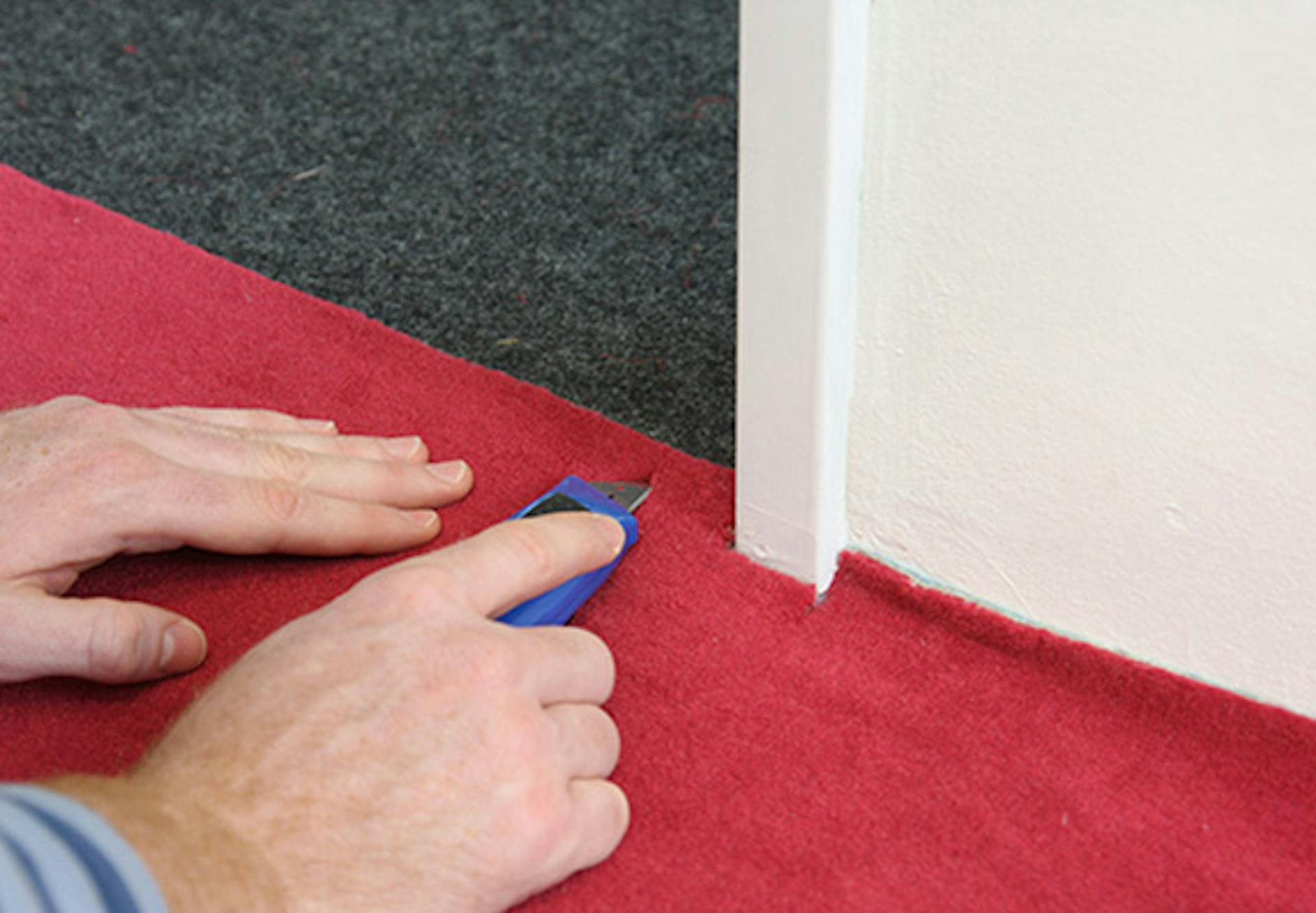 Pracovník orezáva červený koberec pri zárubni a prahu dverí.