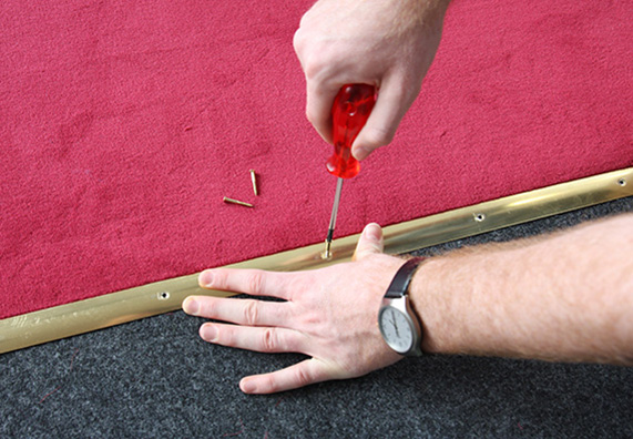 Pracovník upevňuje červený koberec na prechode ku schodom pomocou kovovej lišty.