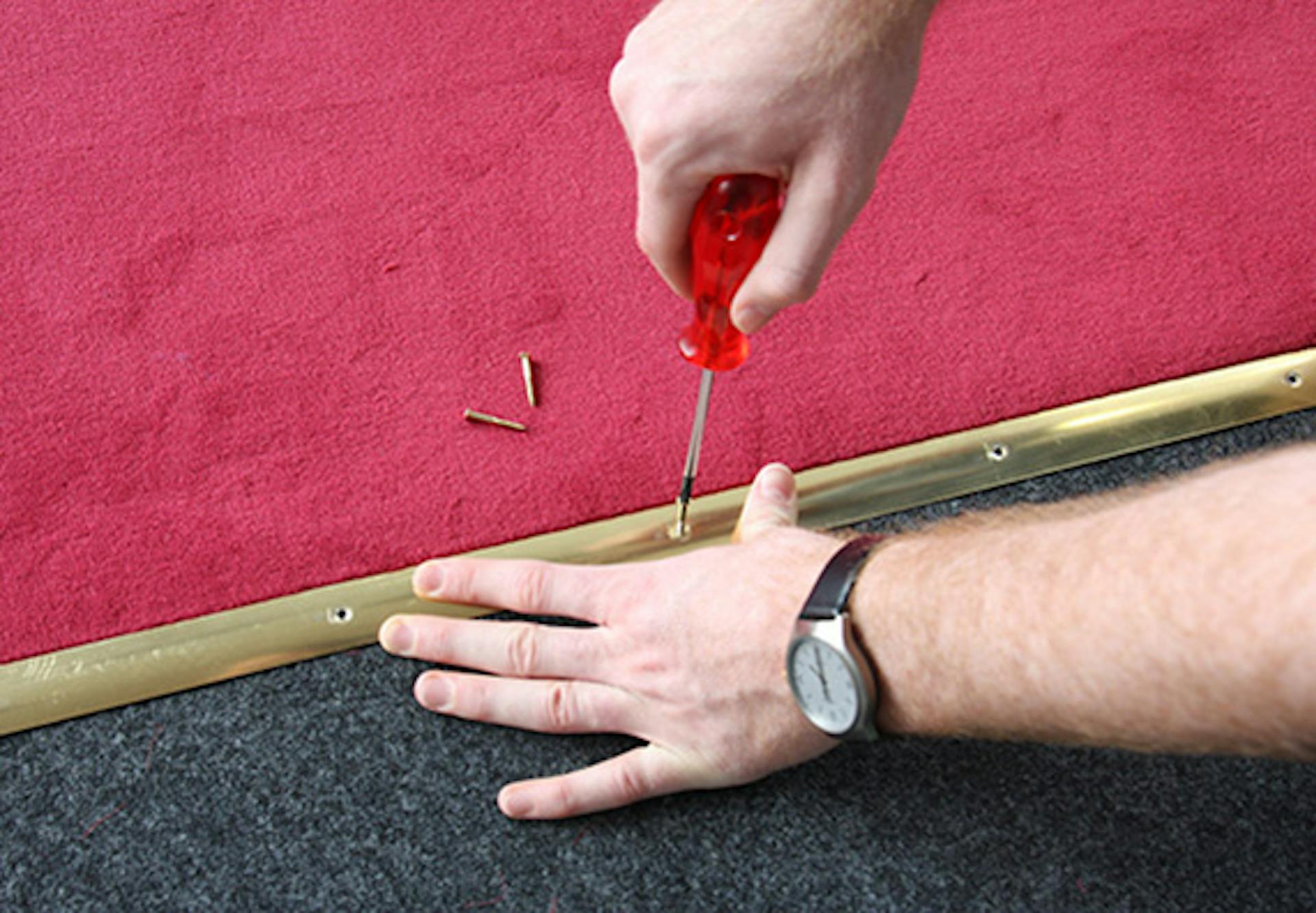 Pracovník upevňuje červený koberec na prechode ku schodom pomocou kovovej lišty.