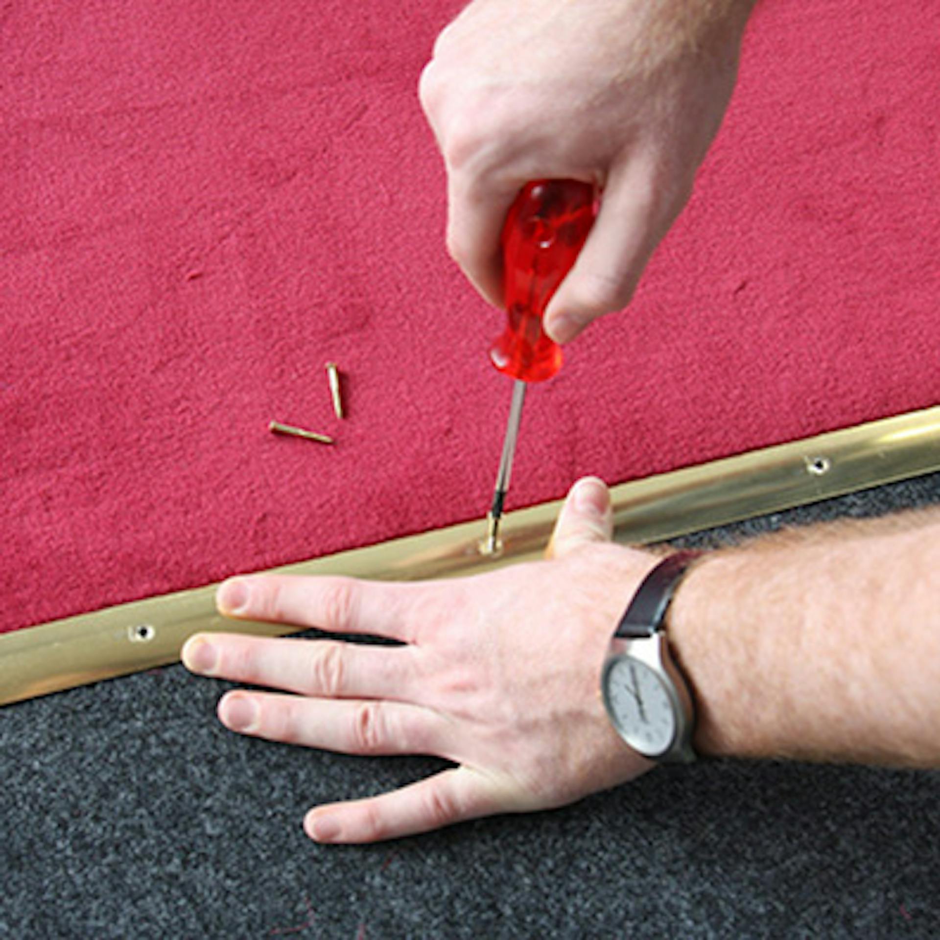 Heimwerker fixiert roten Teppich an Übergang zur Treppe mit Metallschiene.
