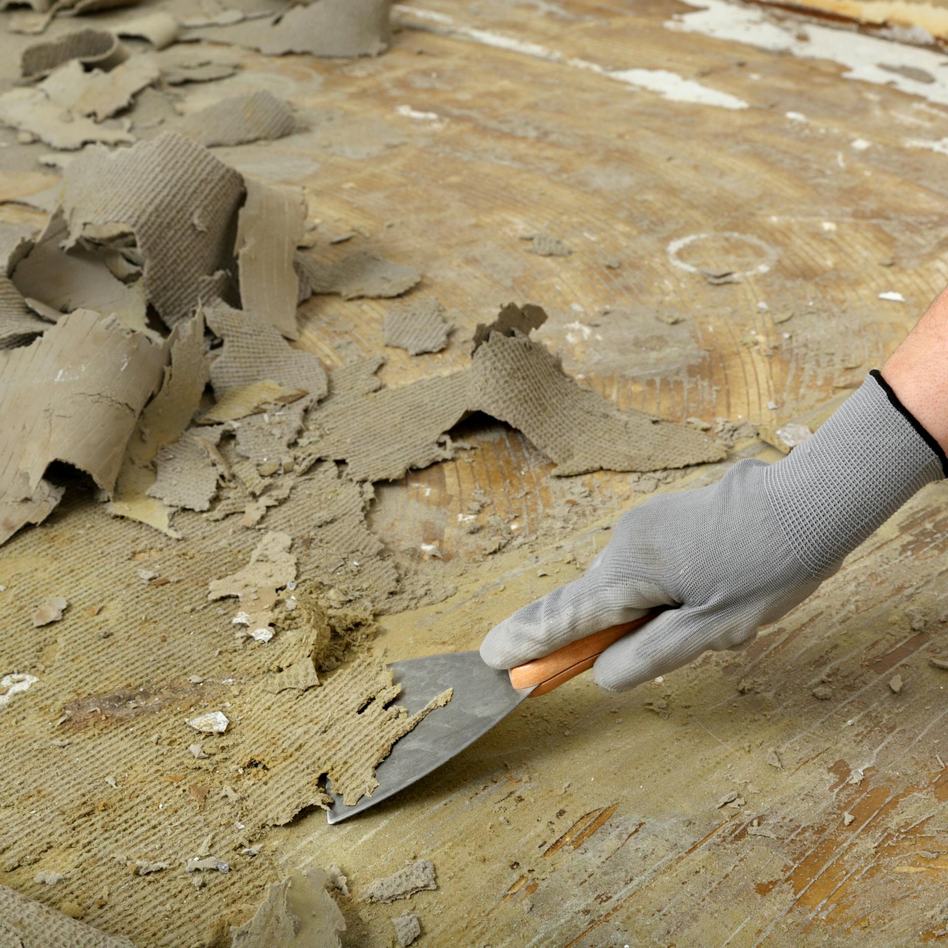 Valaki eltávolítja a padlószőnyeg ragasztómaradványait egy spatulyával