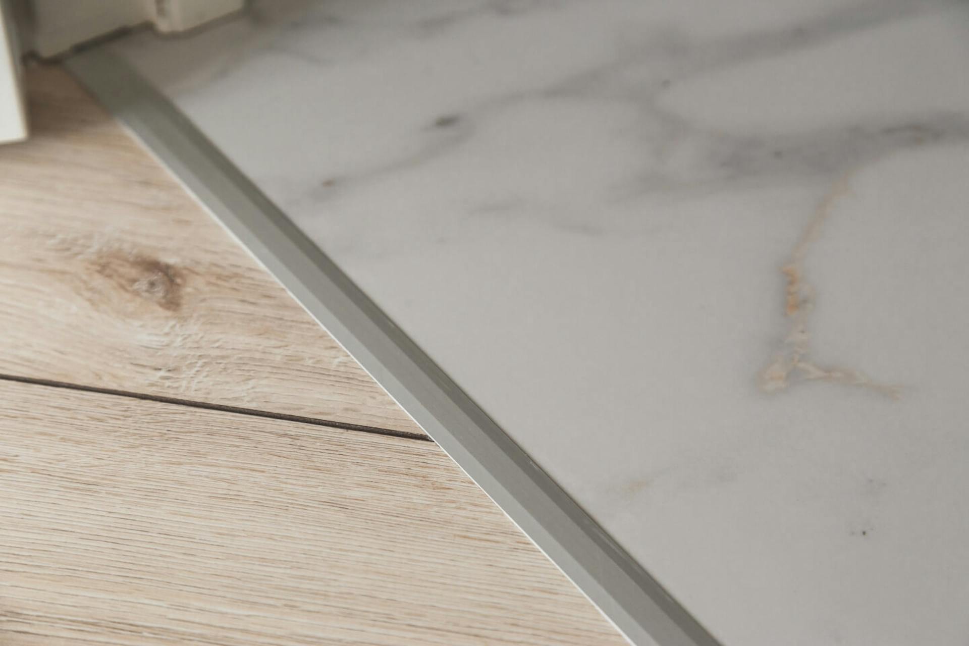 Pavimento in legno chiaro separato dal pavimento in vinile grazie alla guida di raccordo in alluminio.