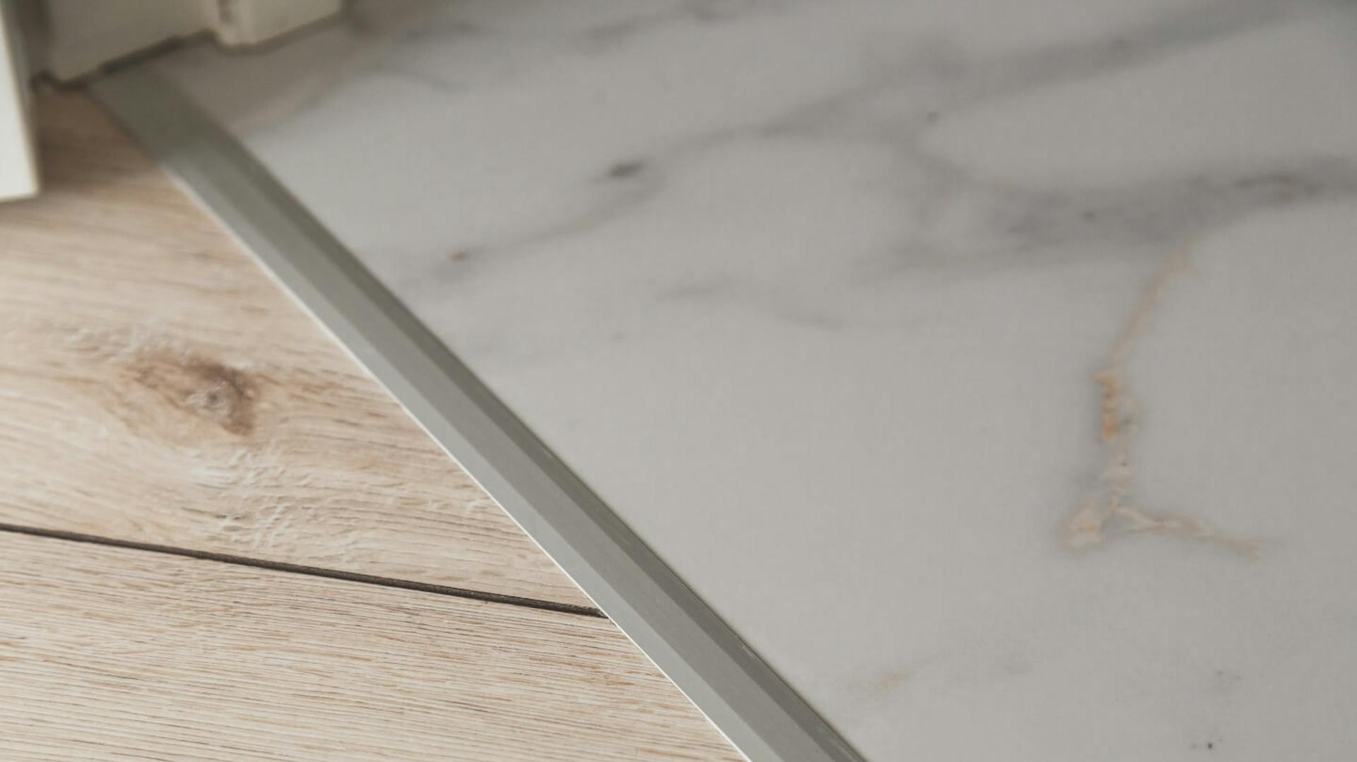 Heller Holzboden durch Aluminium-Übergangsschiene von Vinylboden getrennt.