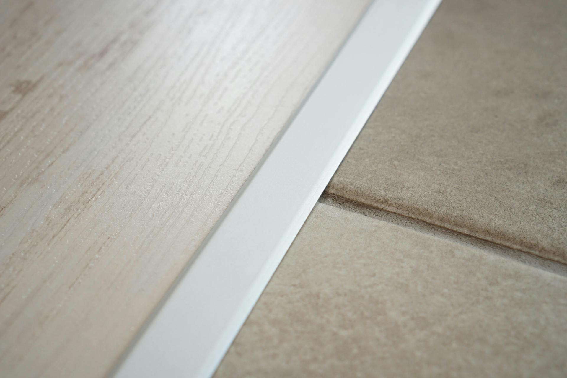 Pavimento in legno separato dal pavimento piastrellato mediante una guida di raccordo bianca.