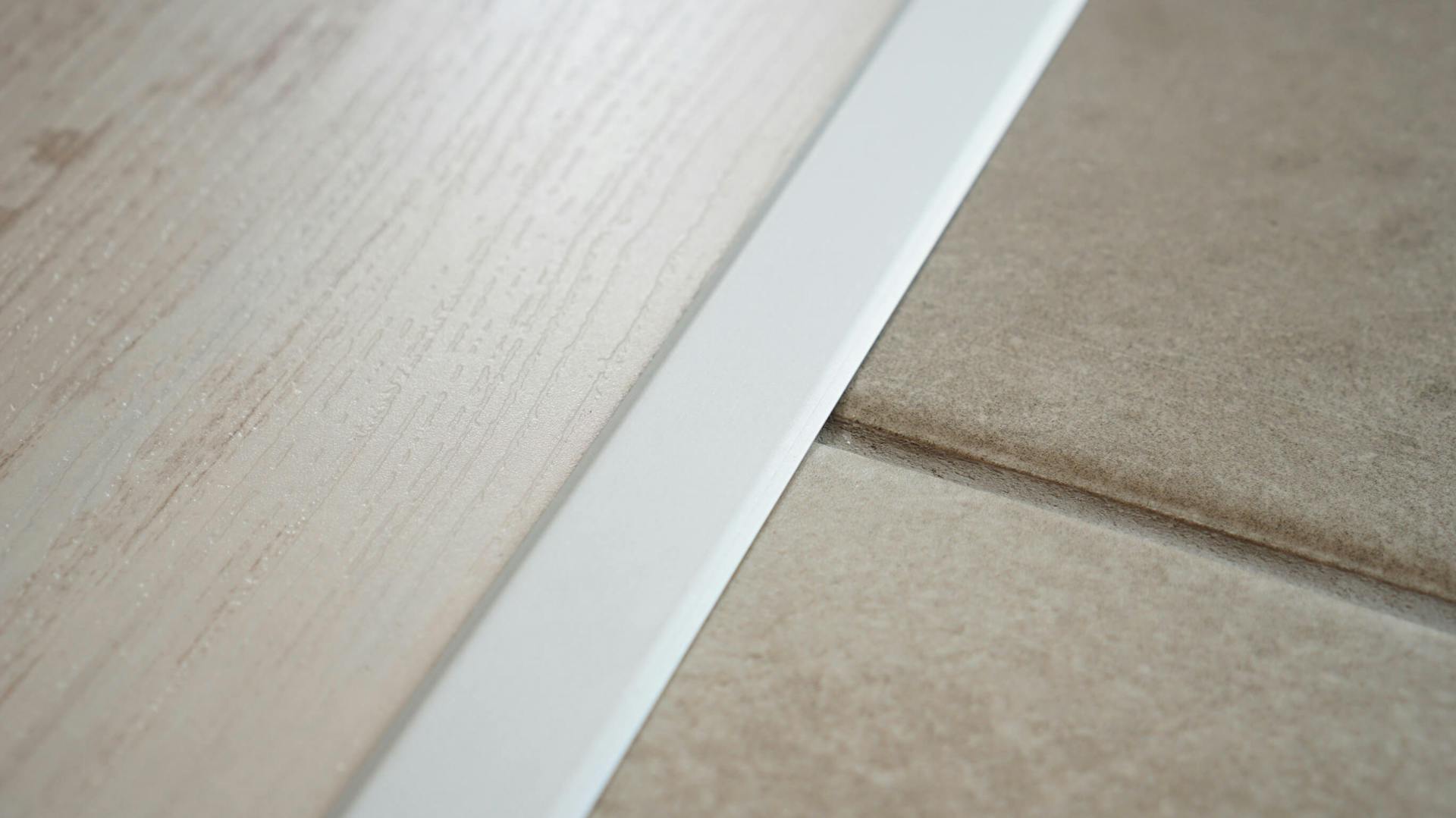 Drevená podlaha oddelená od dlažbovej podlahy bielou prechodovou lištou.