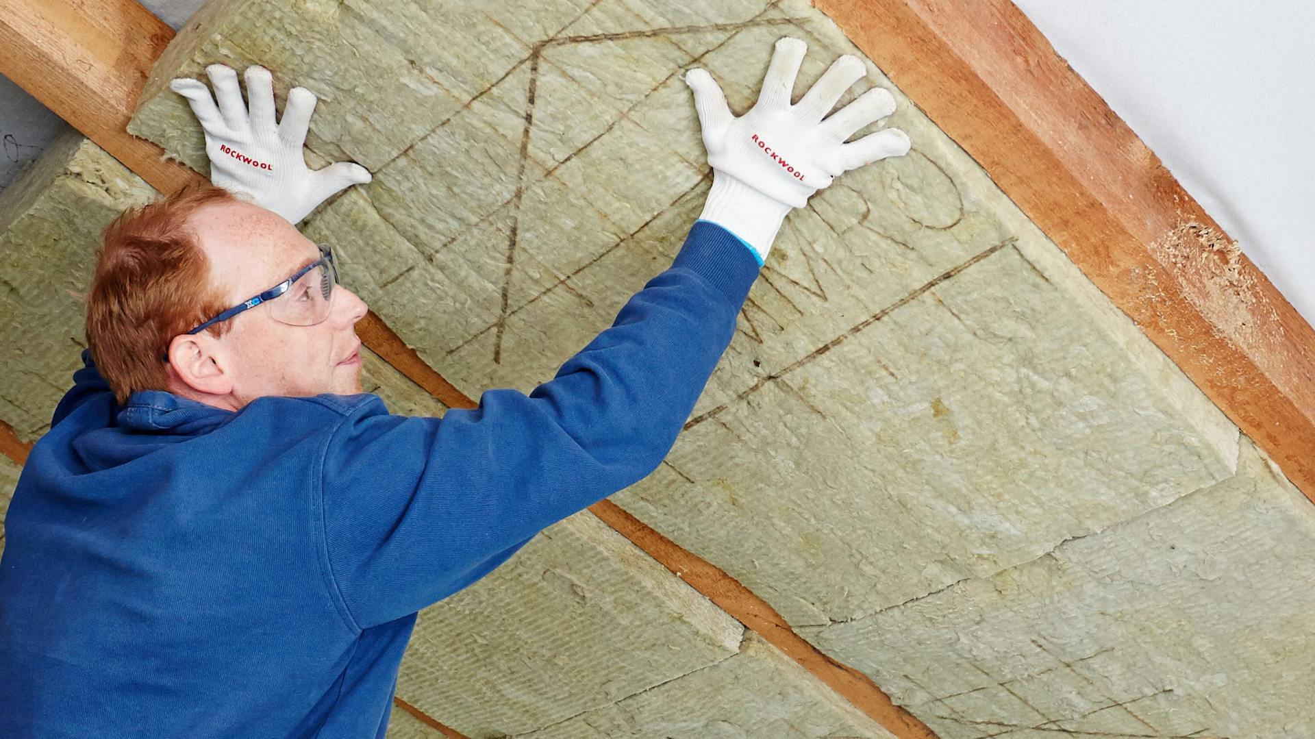 Mann setzt Dämmmaterial zwischen Dachsparren ein.