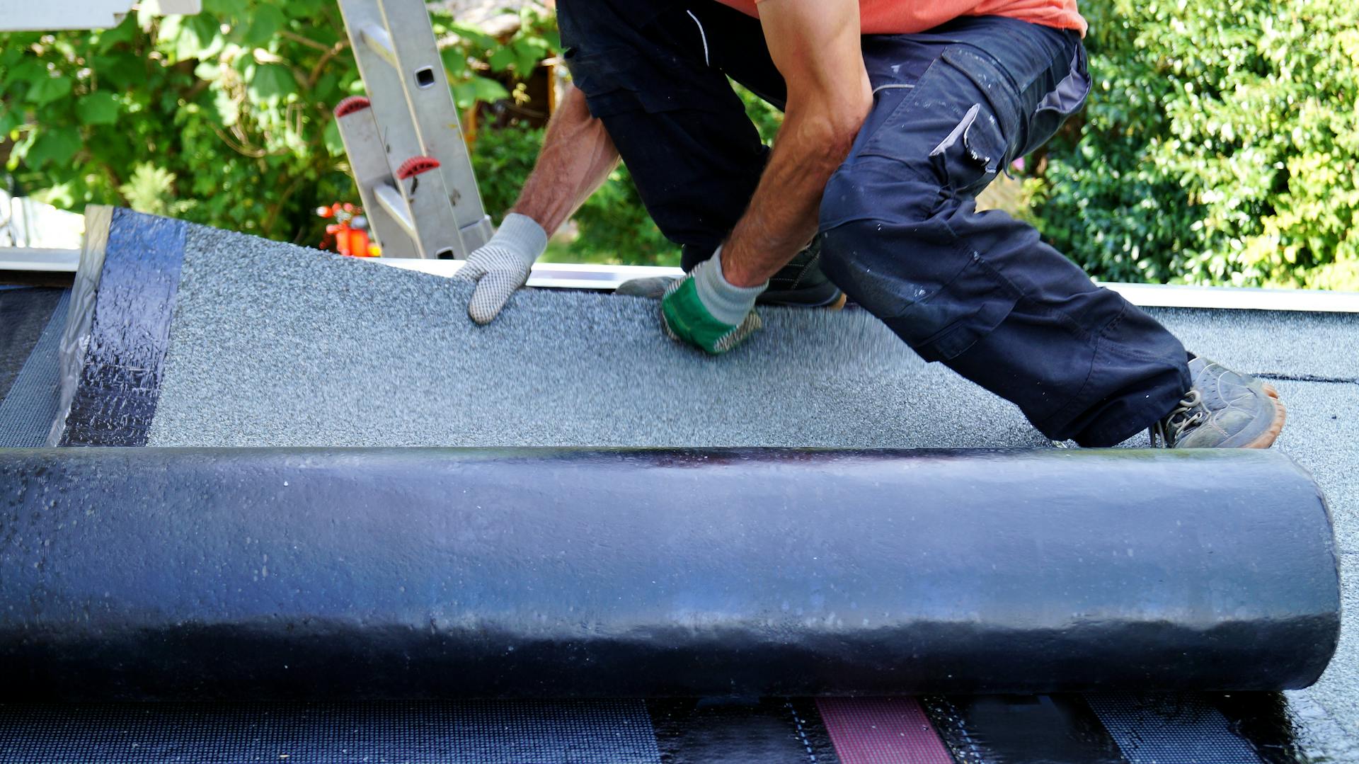 Ein Mann verlegt Dachpappe auf einem Dach.