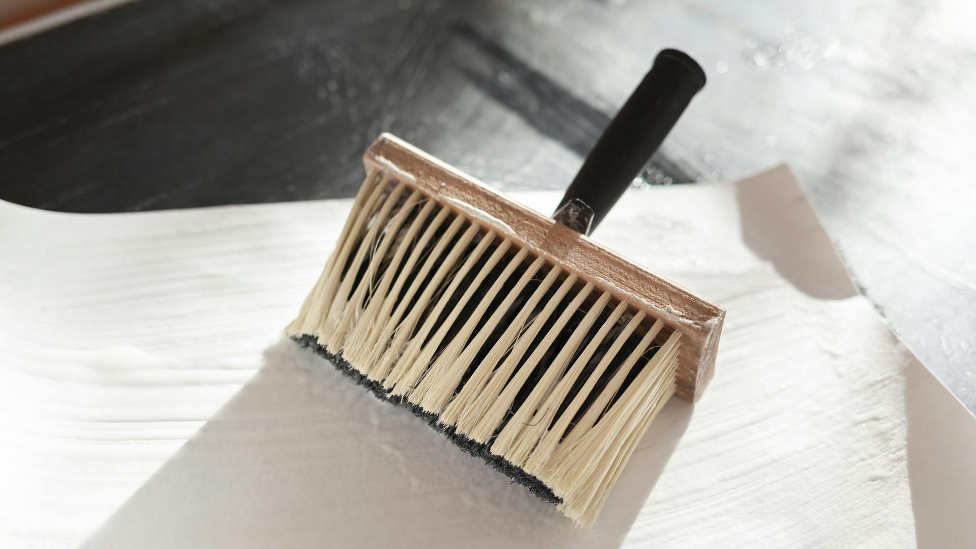 Eine Tapetenbahn mit einem Kleisterquast und Tapetenkleister.