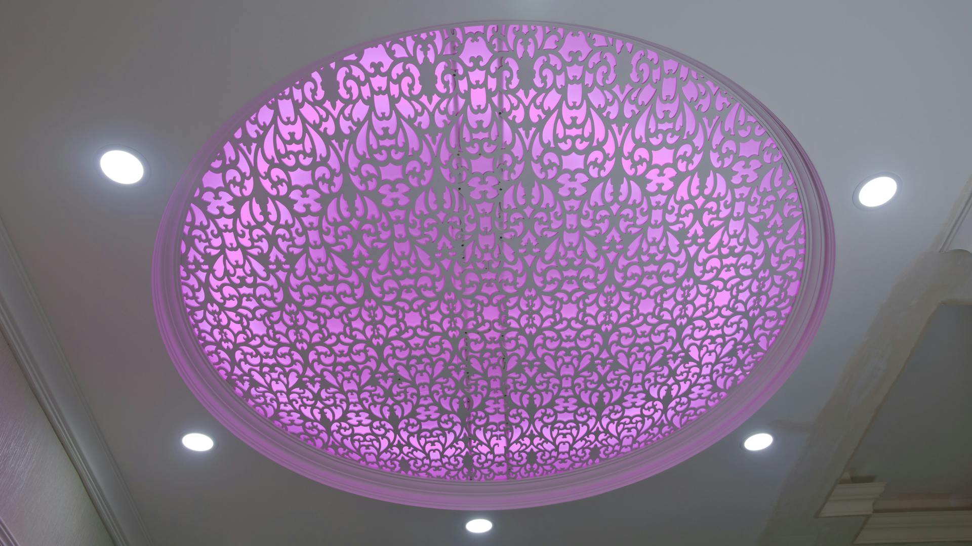 Beleuchtete Spanndecke mit Auslassungen für kleinere Strahler und einer großen, gemusterten Auslassung mit pinker Beleuchtung.