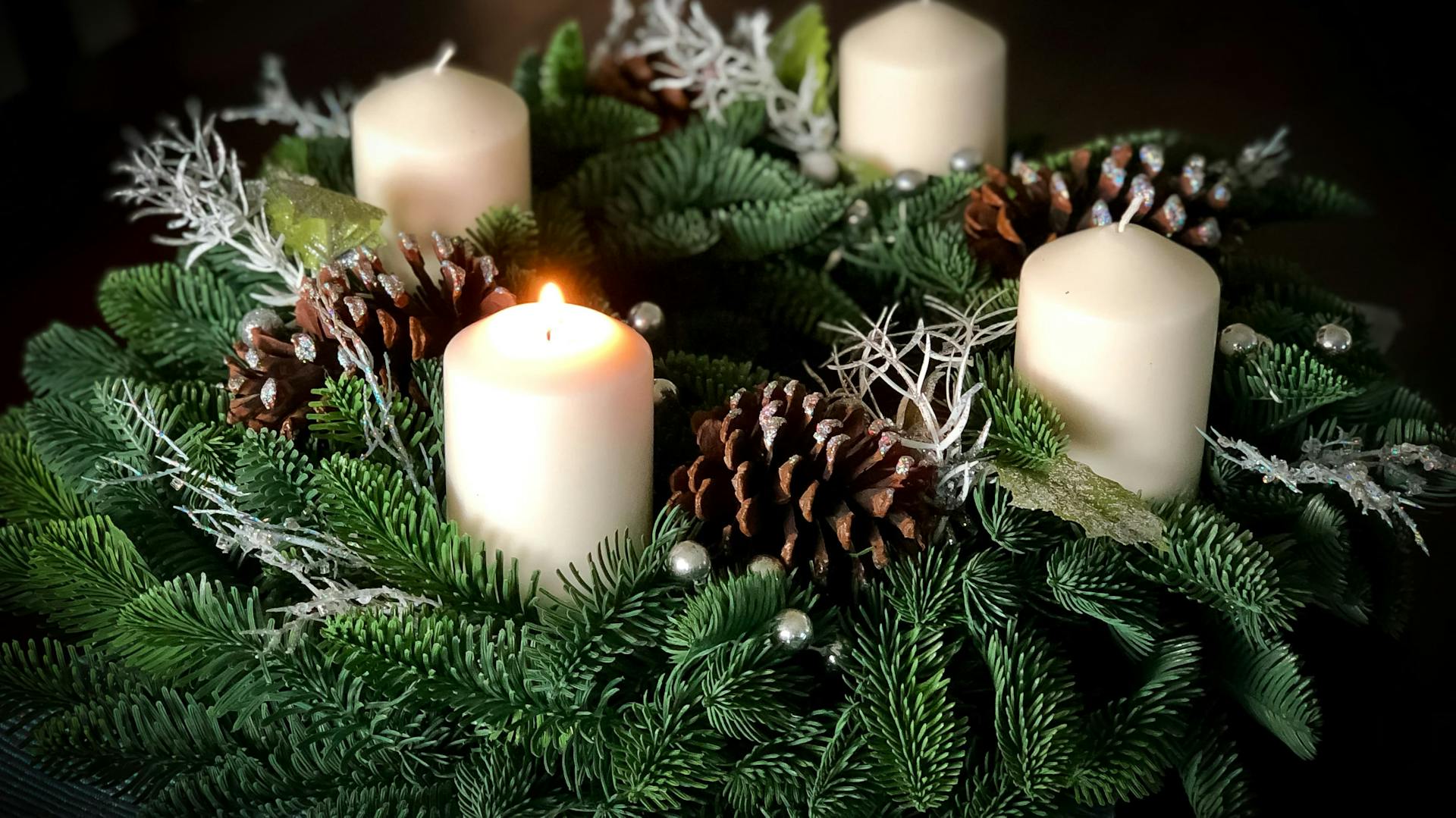 Ein Adventskranz mit weißen Kerzen und weihnachtlicher Dekoration steht auf einem Tisch.