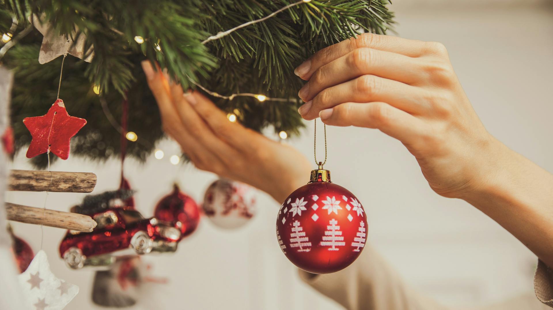 Idee di bricolage per il Natale con istruzioni: ghirlanda per soffitto, decorazione, mano appende una pallina all'albero di Natale