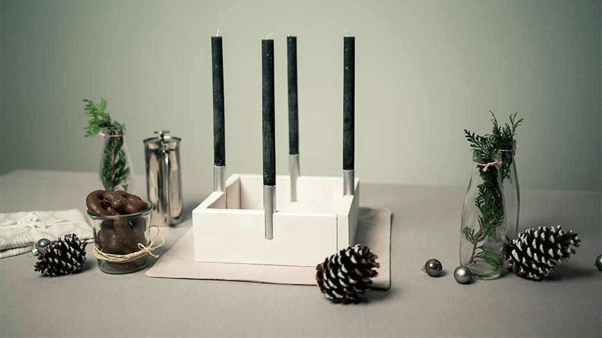Vassoio quadrato bianco con quattro candele lunghe nere come corona dell’Avvento moderna sul tavolo