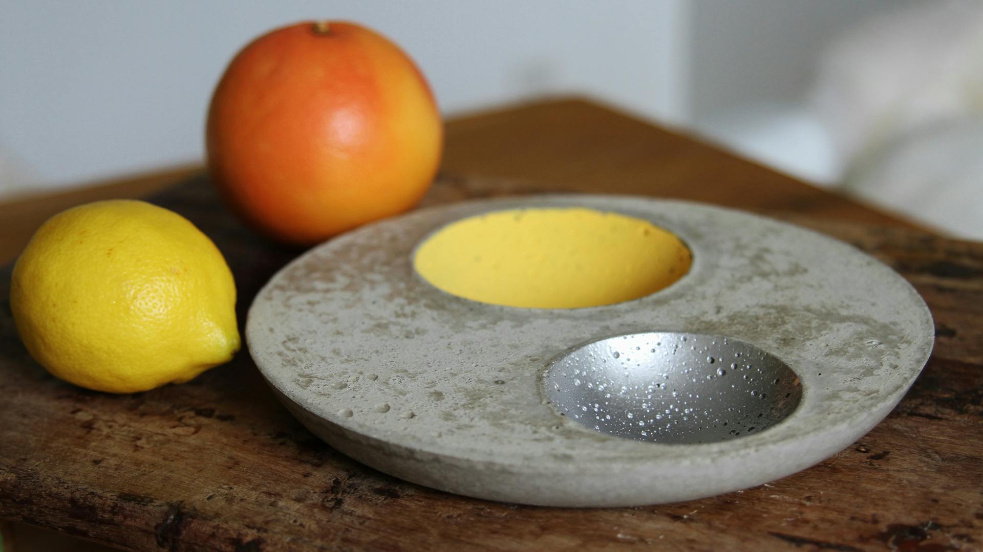 Obstschale aus Bastelbeton auf Holztisch neben Orange und Zitrone