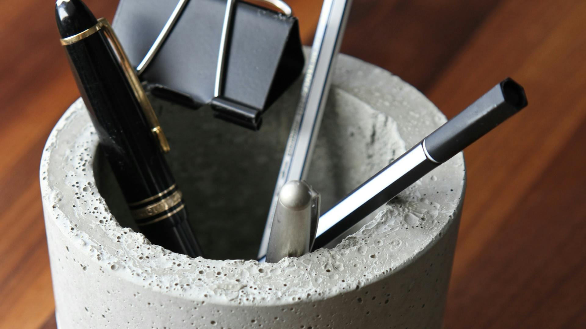 Stiftebecher aus Bastelbeton mit Stiften und Dokumentenklammer auf Holztisch