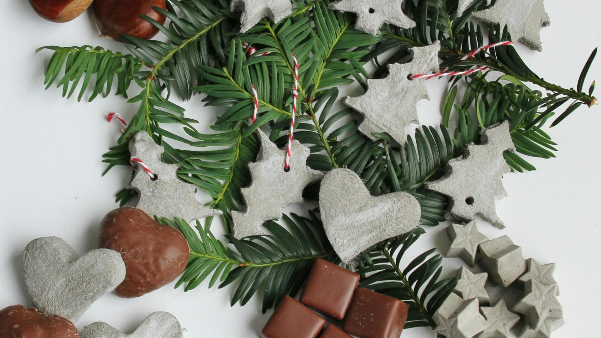 Weihnachtliche Streudekoration aus Knetbeton in Tannenbaumform und Herzform an Dominosteinen und Lebkuchenherzen und Kastanien und Tannenzweigen auf Tisch