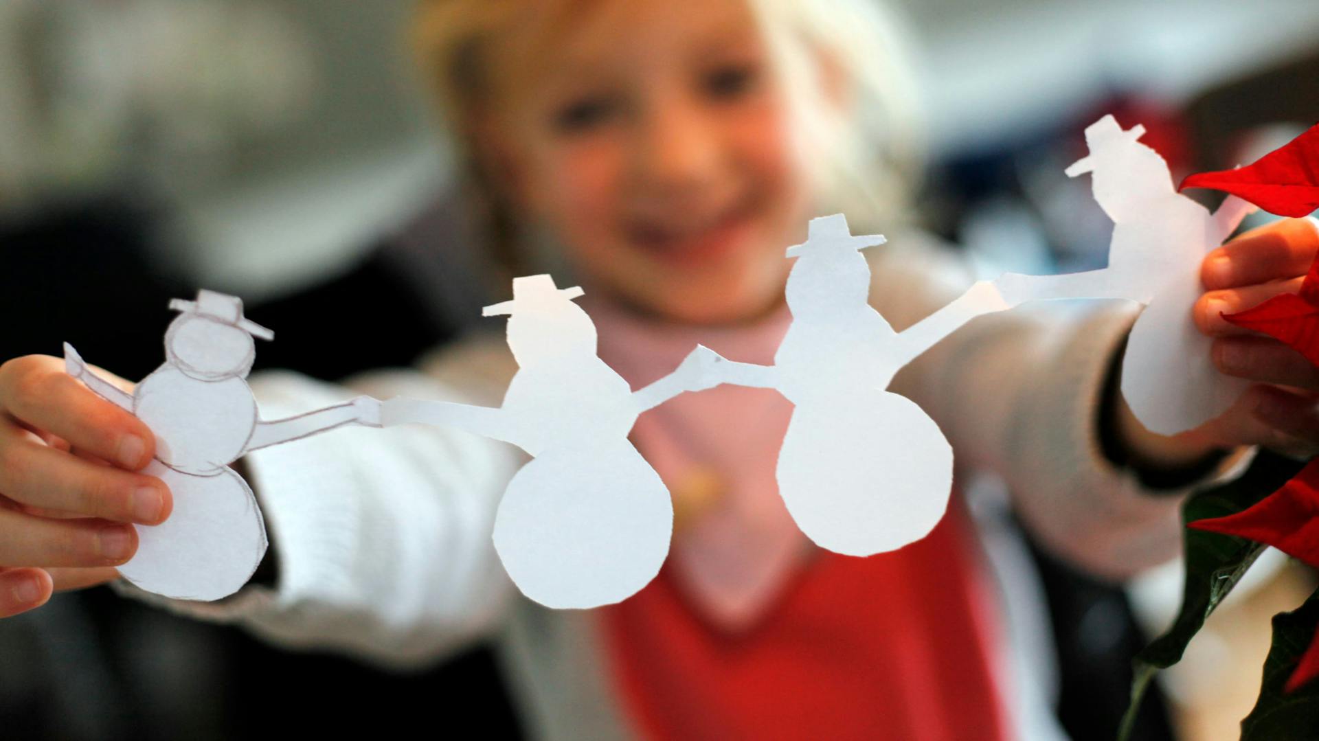 Ein Mädchen hält eine Schneemann-Girlande aus Papier hoch.