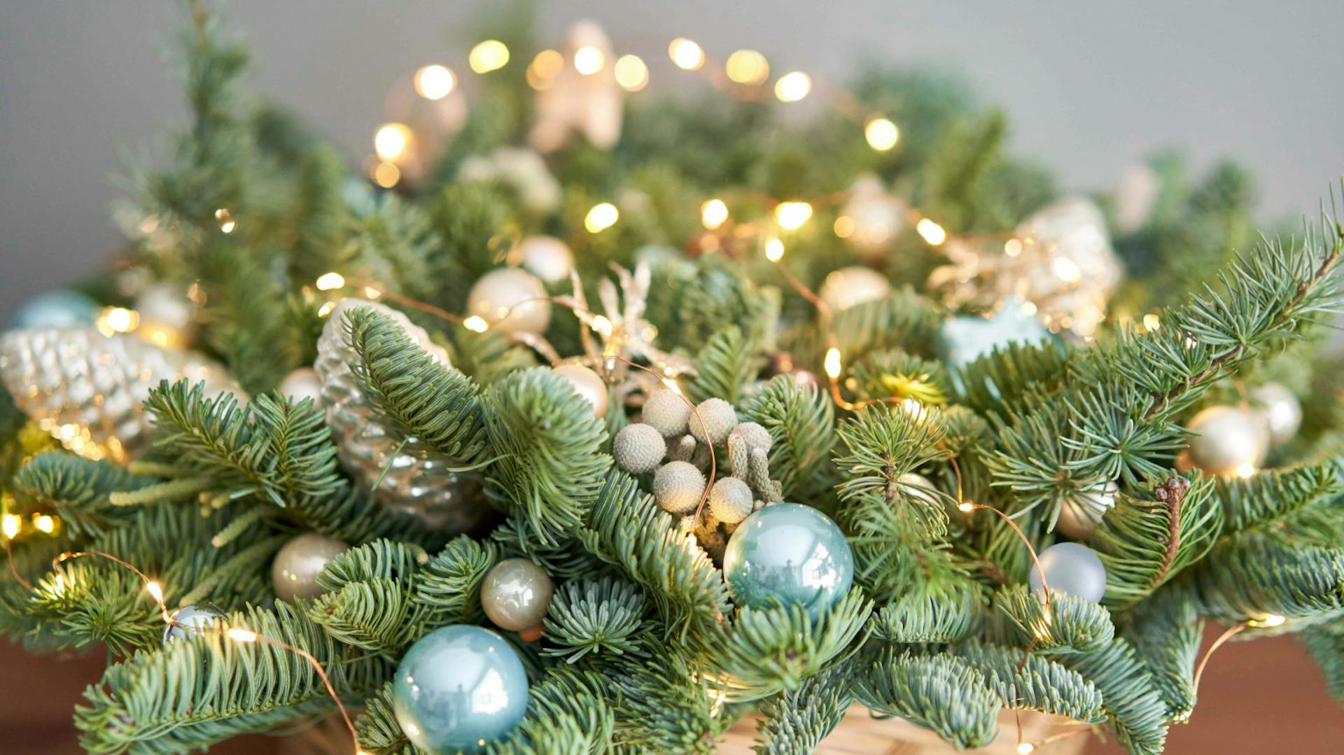 Composizione dell’Avvento in cesto con ramoscelli d’abete, ghirlanda luminosa e piccole palline di Natale blu