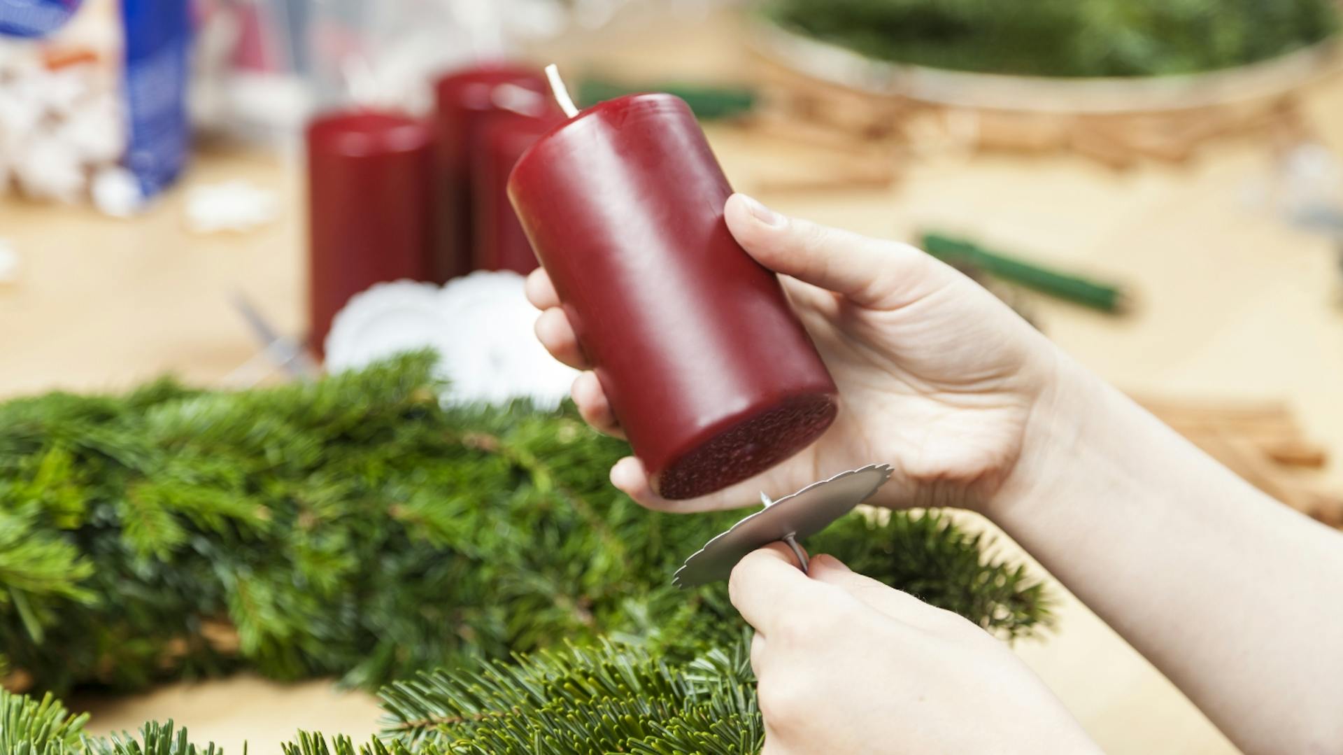 Jemand befestigt eine Kerze an einem Adventskranz.