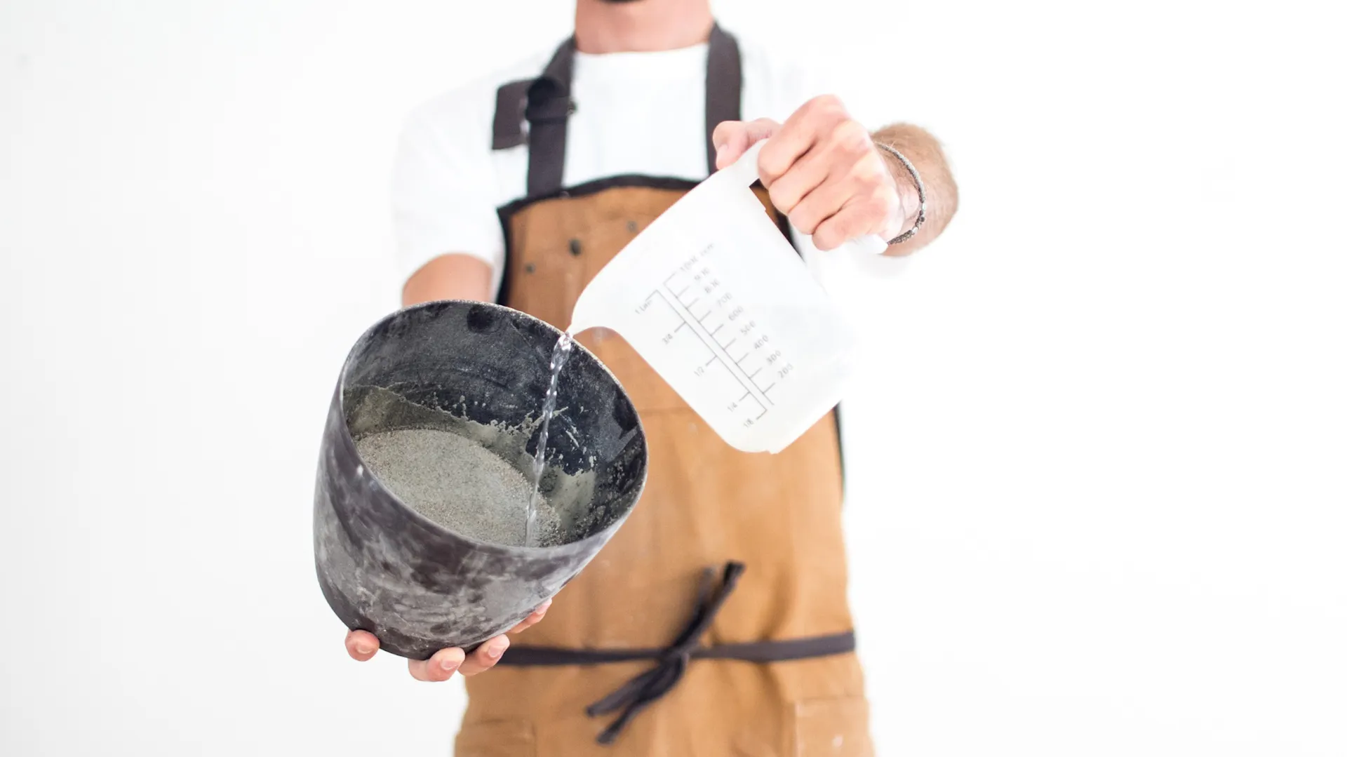 Mann in Schürze mischt Beton mit Wasser in Becher an