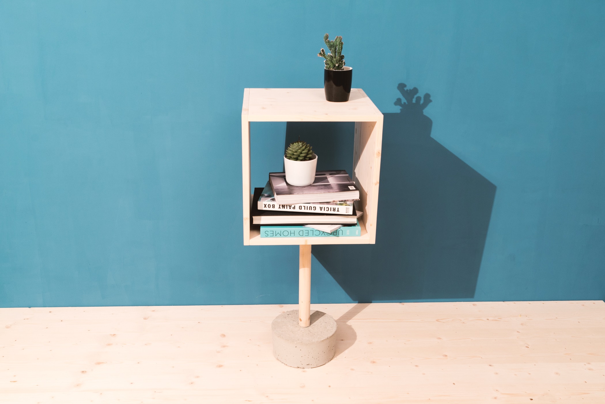 Sideboard mit Betonfuß auf Holzboden vor türkiser Wand