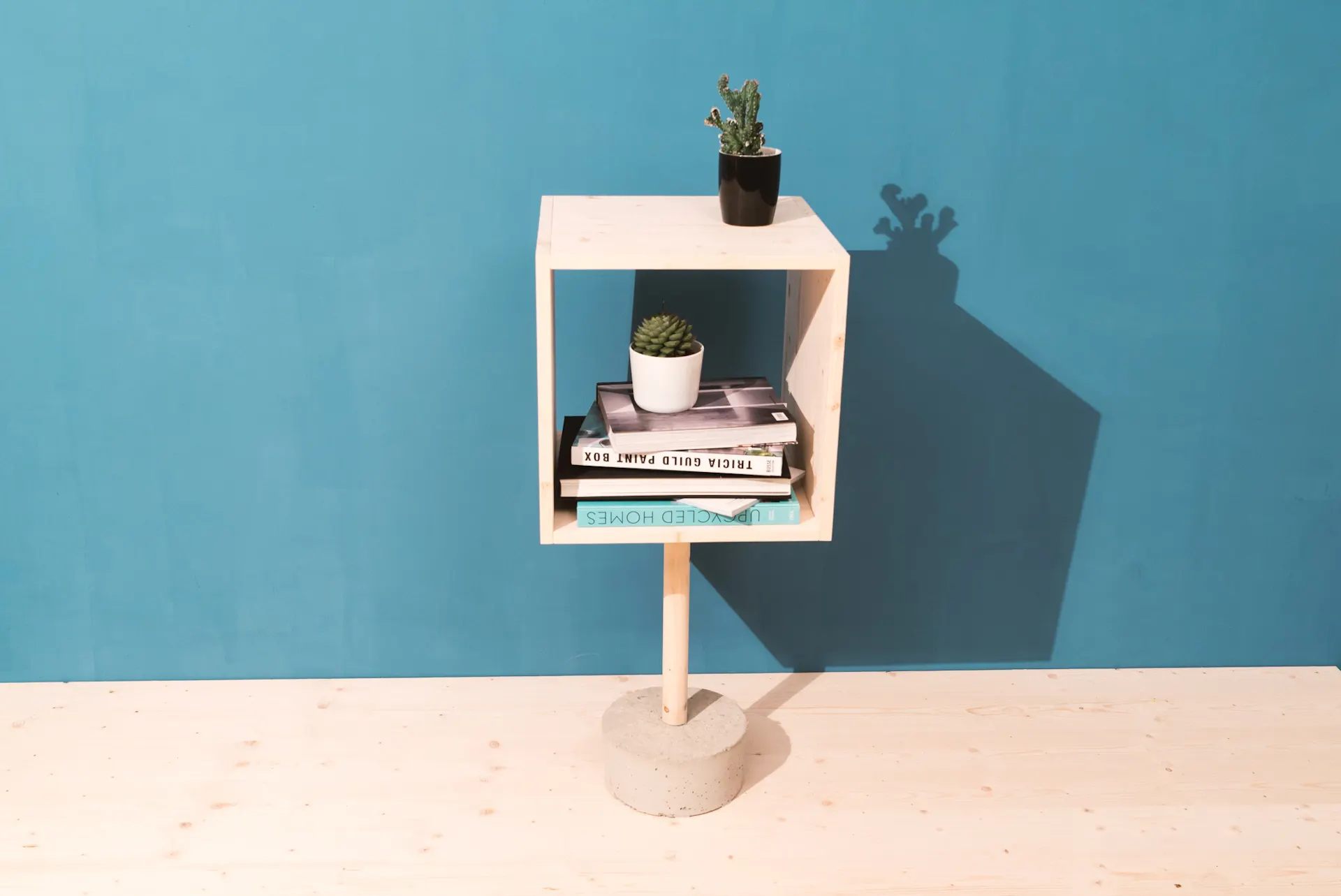 Sideboard mit Betonfuß auf Holzboden vor türkiser Wand