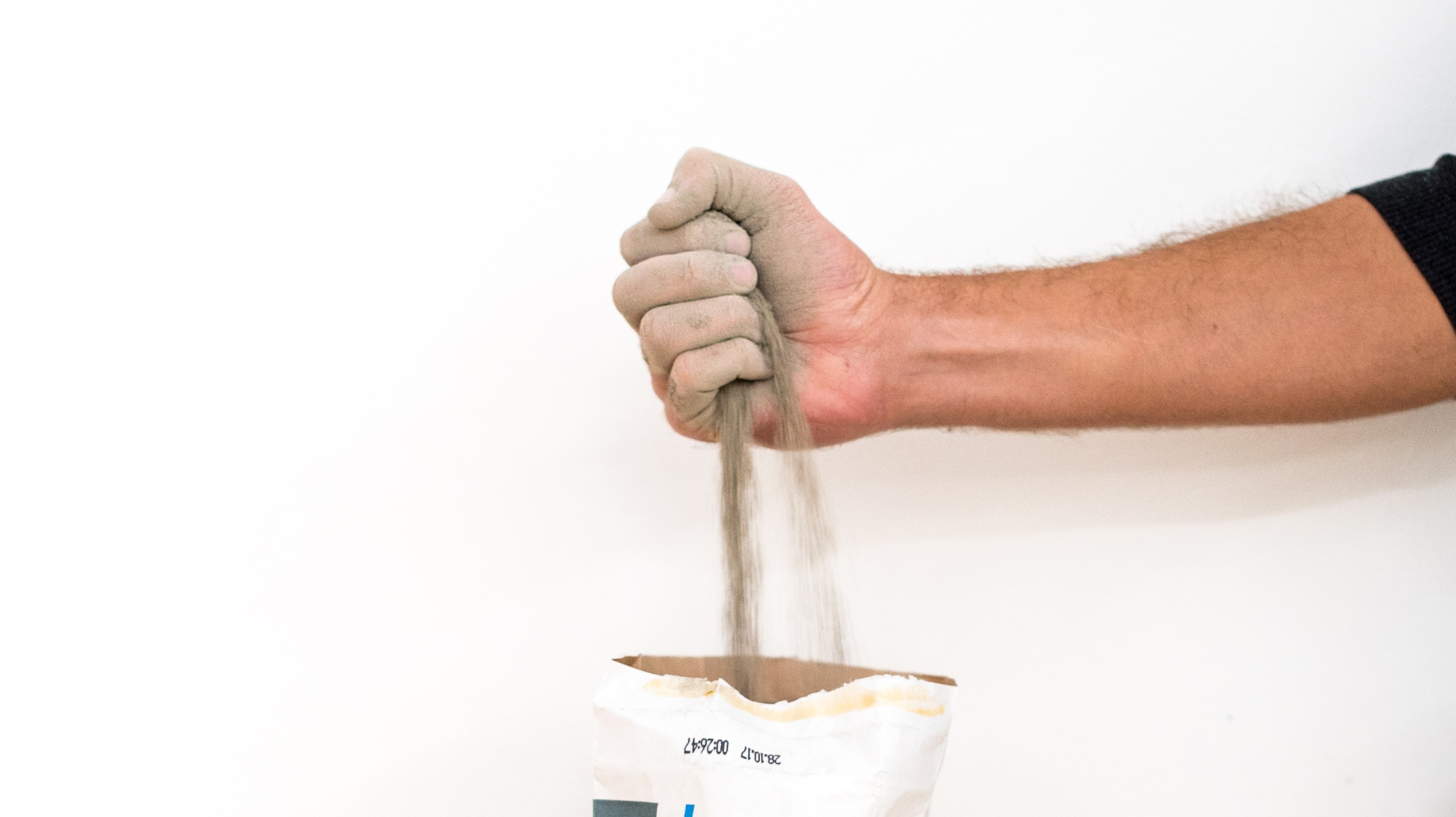 Trockener Beton rieselt durch eine Hand in eine Tüte.