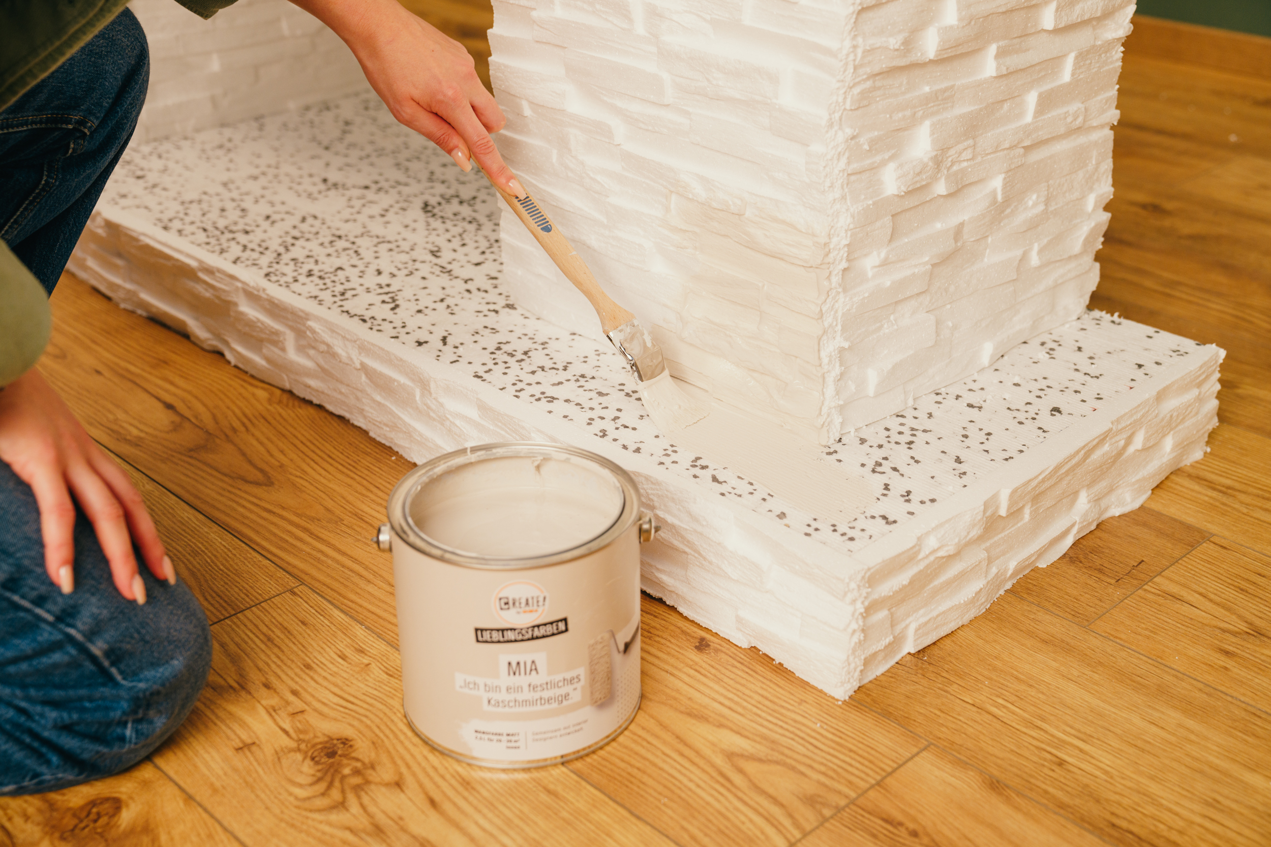 Egy barkácsoló fehérre fest egy kandallót.