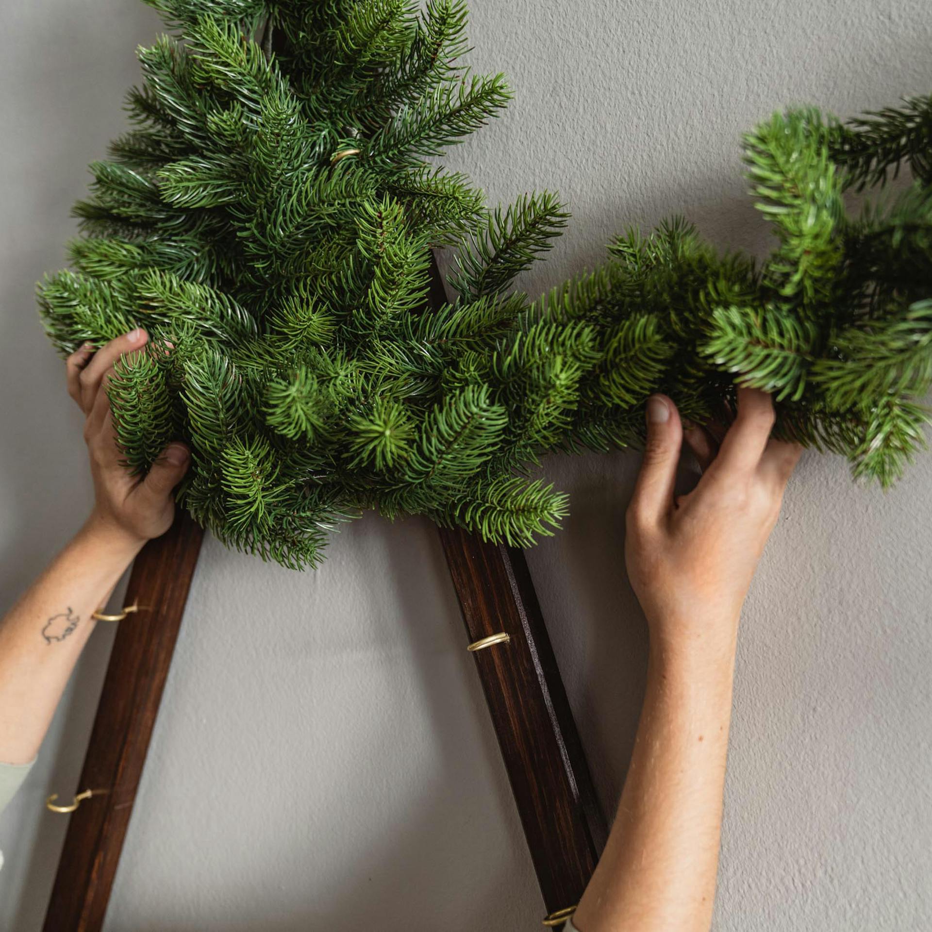 Handwerkerin wickelt eine Tannengirlande um den Rahmen des Wandbaums.