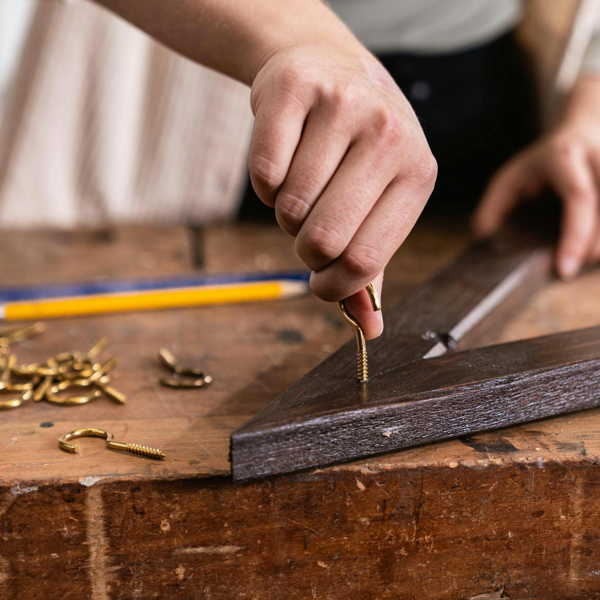 Handwerkerin schraubt Schraubhaken an die Spitze des Wandbaum-Rahmens.