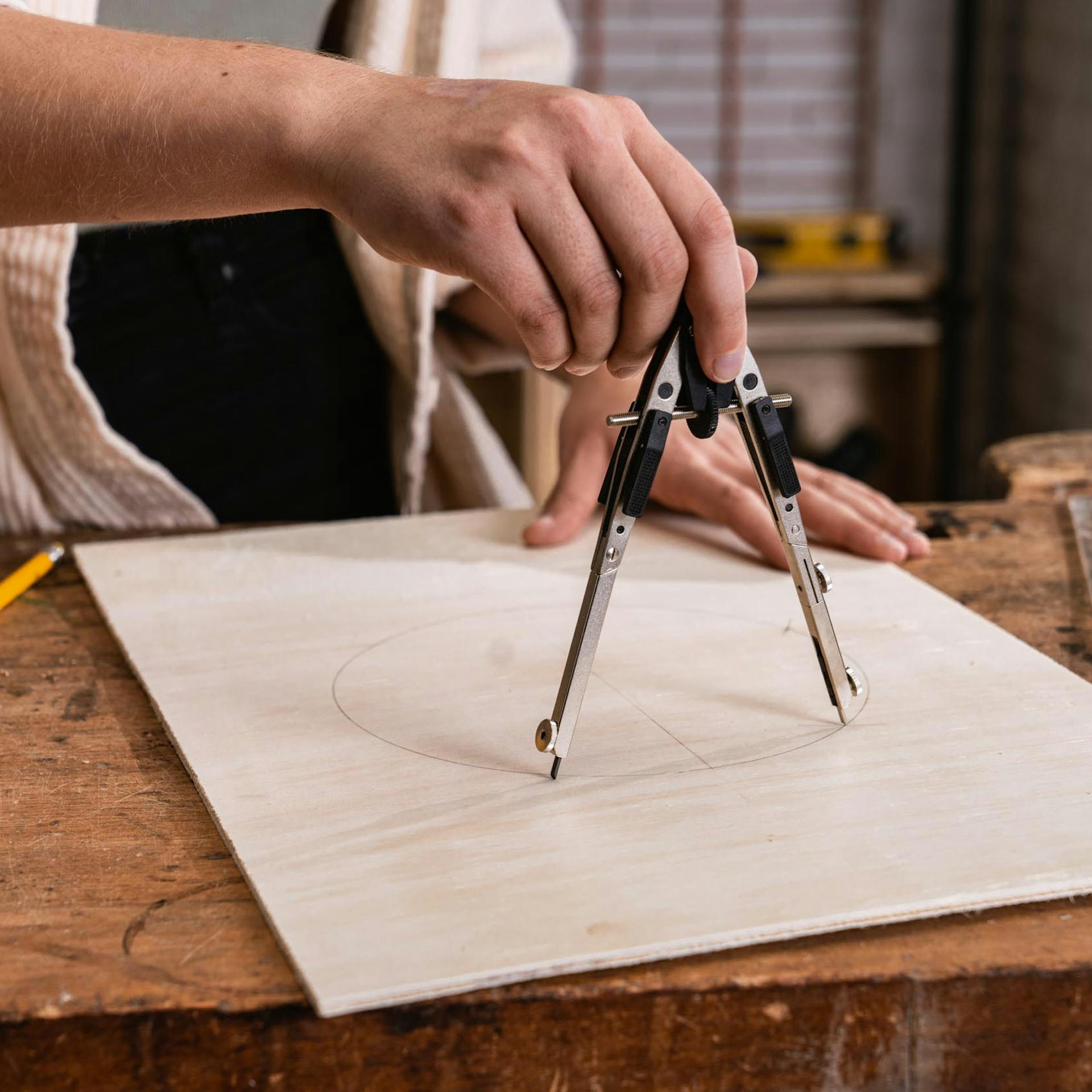 Handwerkerin malt mit einem Zirkel einen Kreis auf eine Sperrholzplatte.