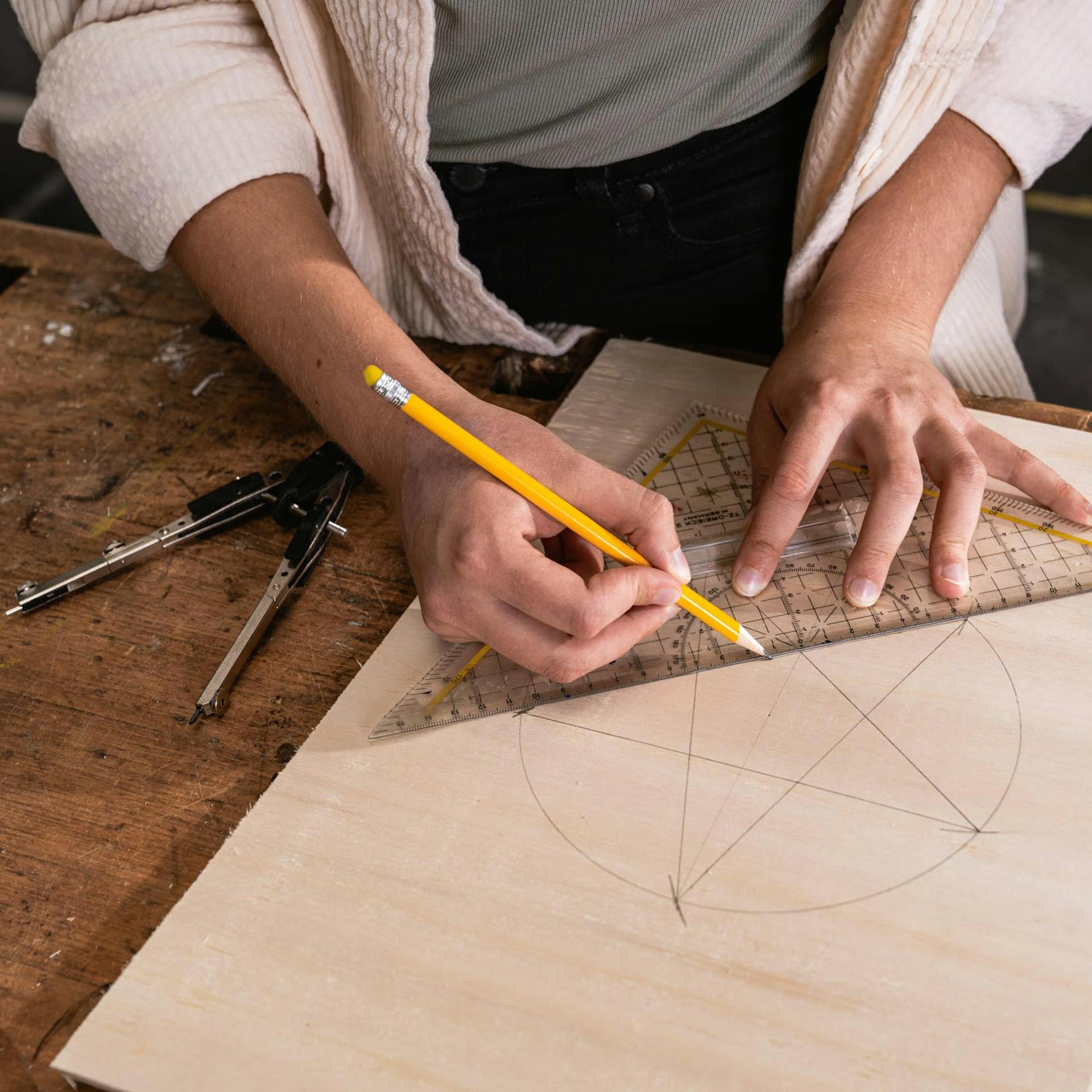 Handwerkerin verbindet mithilfe eines Geodreiecks verschiedene Punkte auf einer Bastelsperrholz-Platte, sodass ein Stern zu erkennen ist.