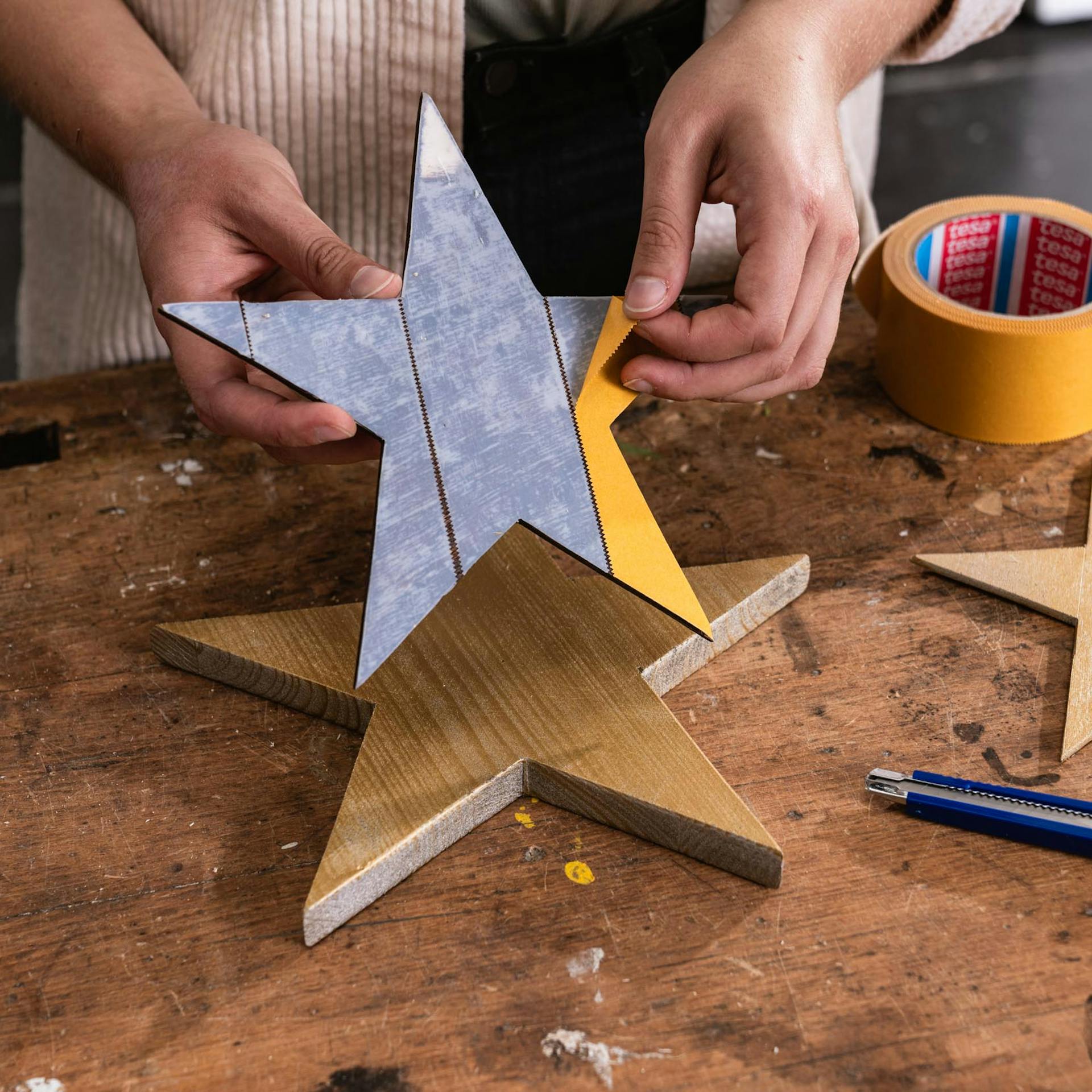 Handwerkerin zieht doppelseitiges Klebeband von einem Holzstern ab.