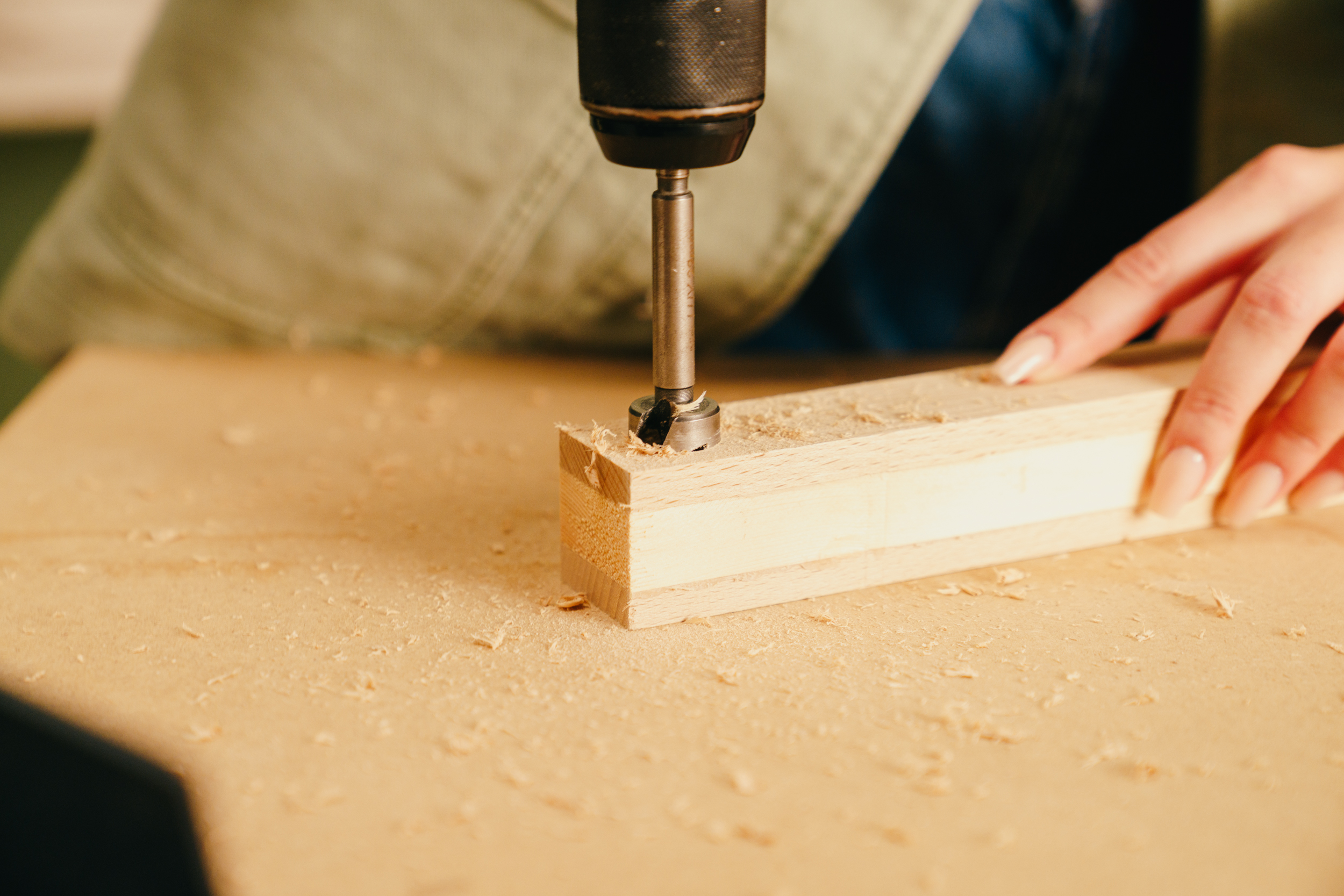 Egy barkácsoló lyukat fúr a lécekbe egy kivetőpánthely fúróval.