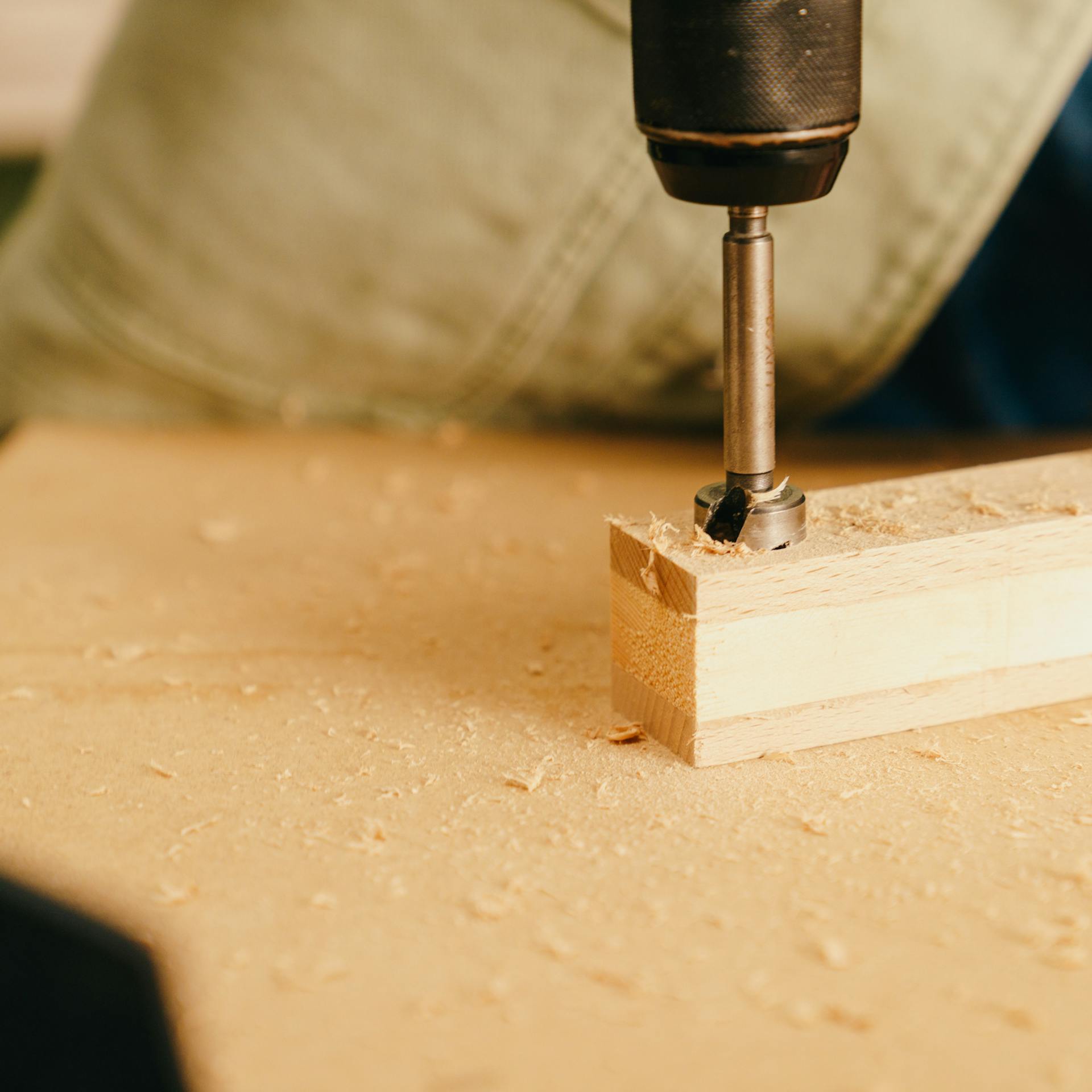 Egy barkácsoló lyukat fúr a lécekbe egy kivetőpánthely fúróval.