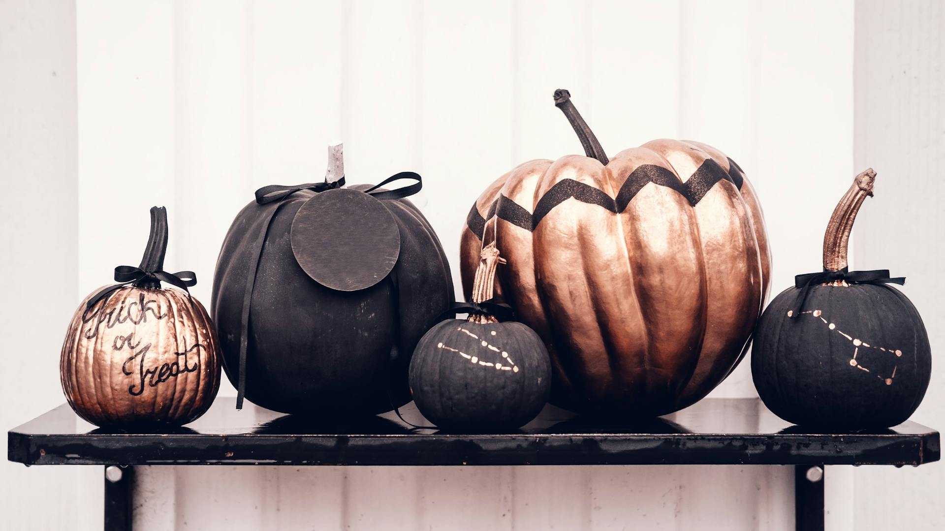 Schwarz und roségold bemalte Kürbisse auf einem schwarzen Wandregal.