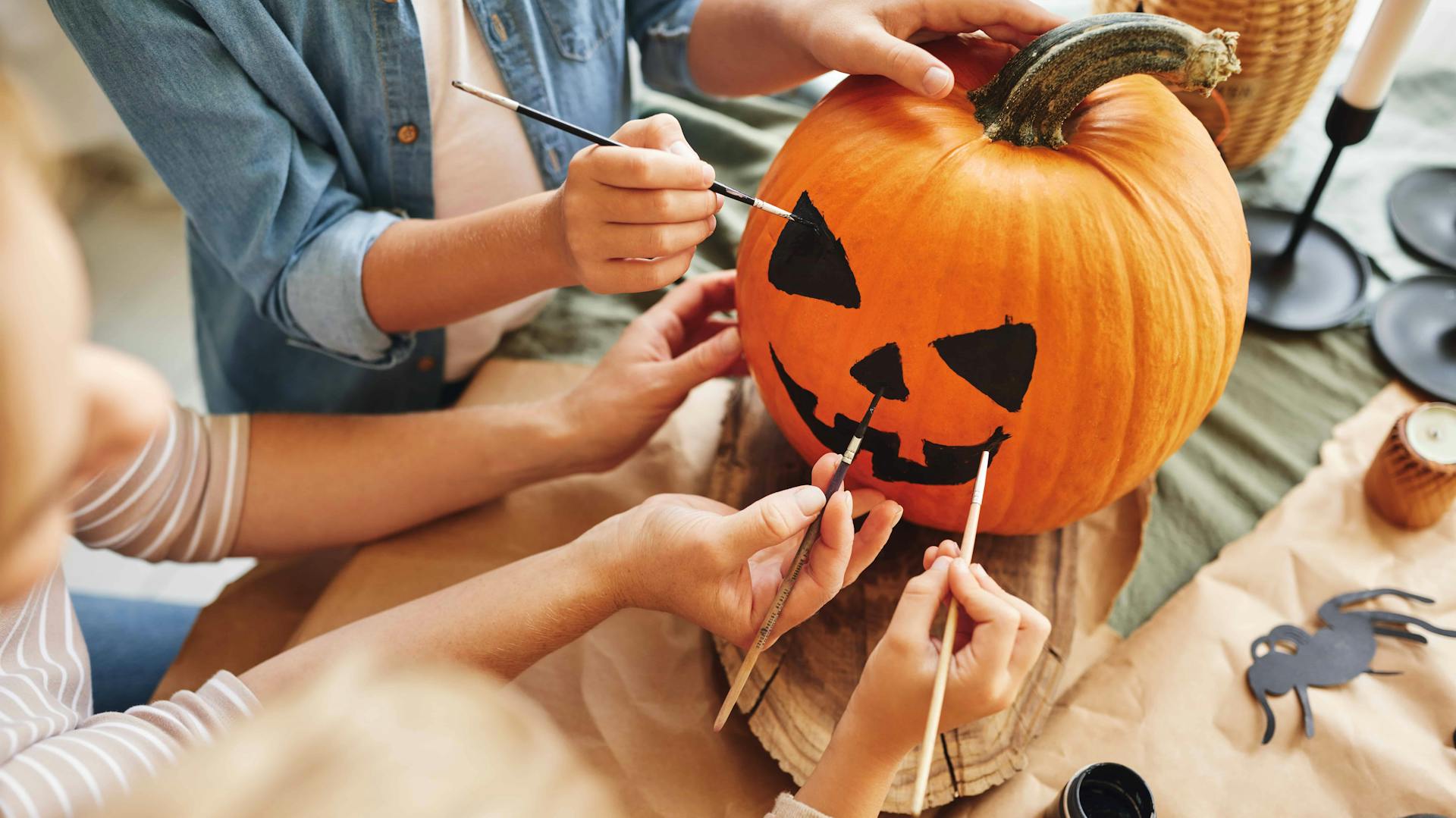 Mehrere Personen bemalen gemeinsam einen Halloween-Kürbis.