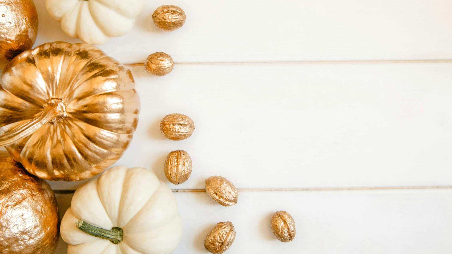 Weiße Kürbisse und mit Gold bemalte Kürbisse neben mit Gold bemalten Walnüssen