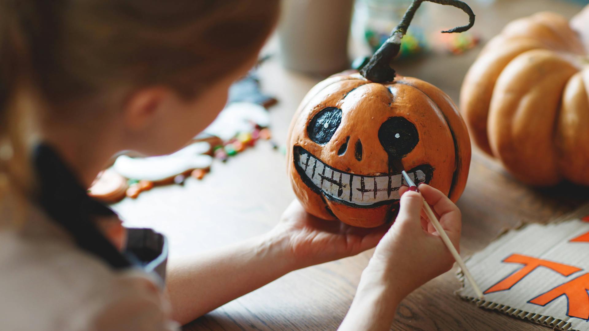 Jemand malt ein Halloween-Gesicht auf einen Kürbis.