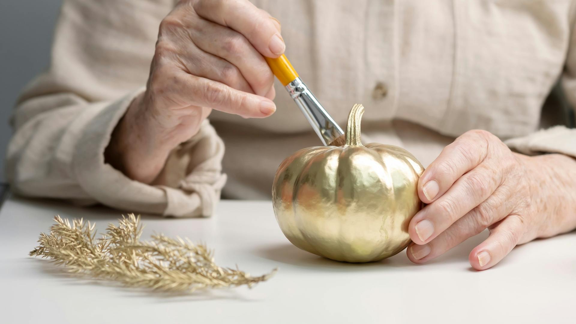 Jemand bemalt einen kleinen Kürbis mit goldener Farbe.