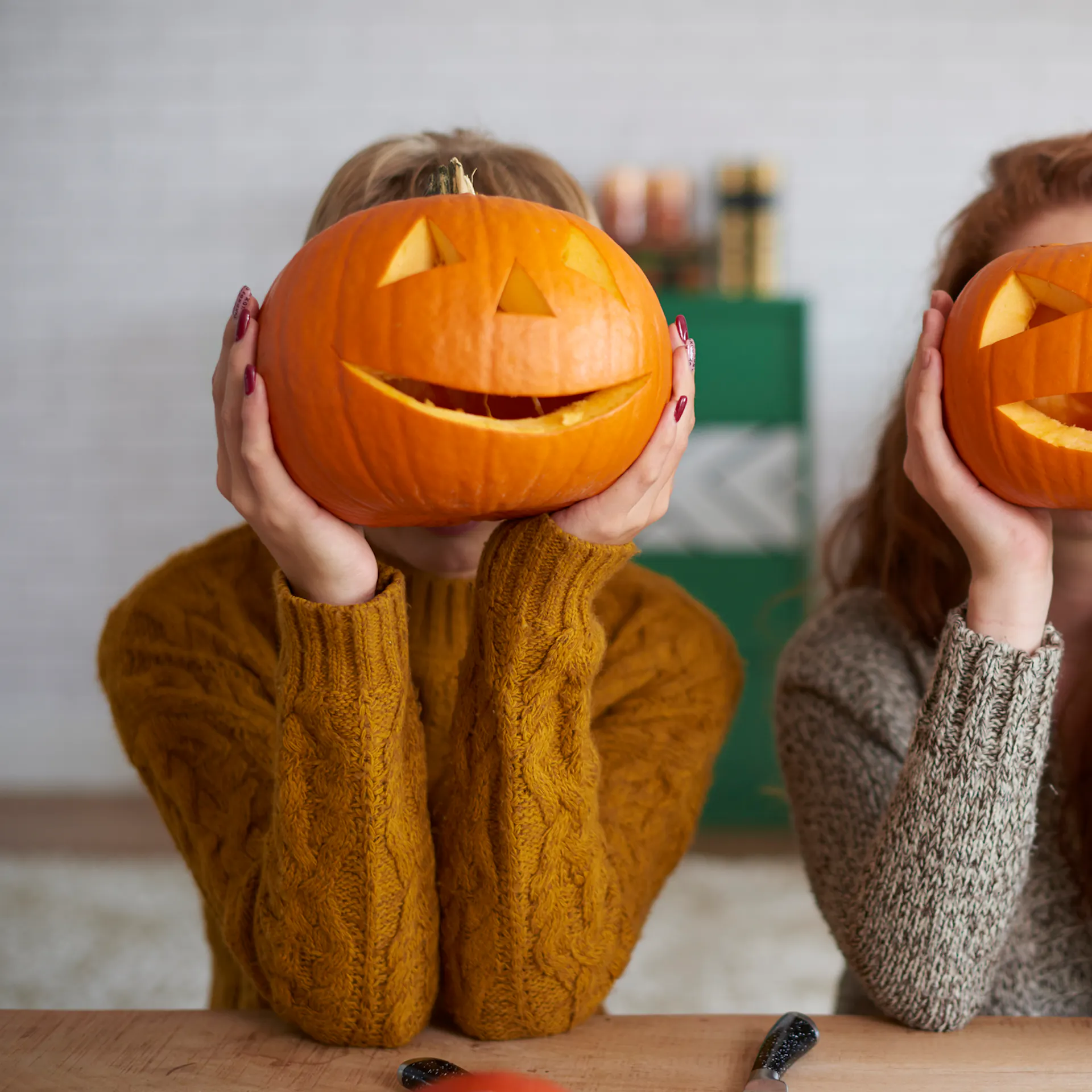 Deux femmes tiennent des courges sculptées devant leur visage.