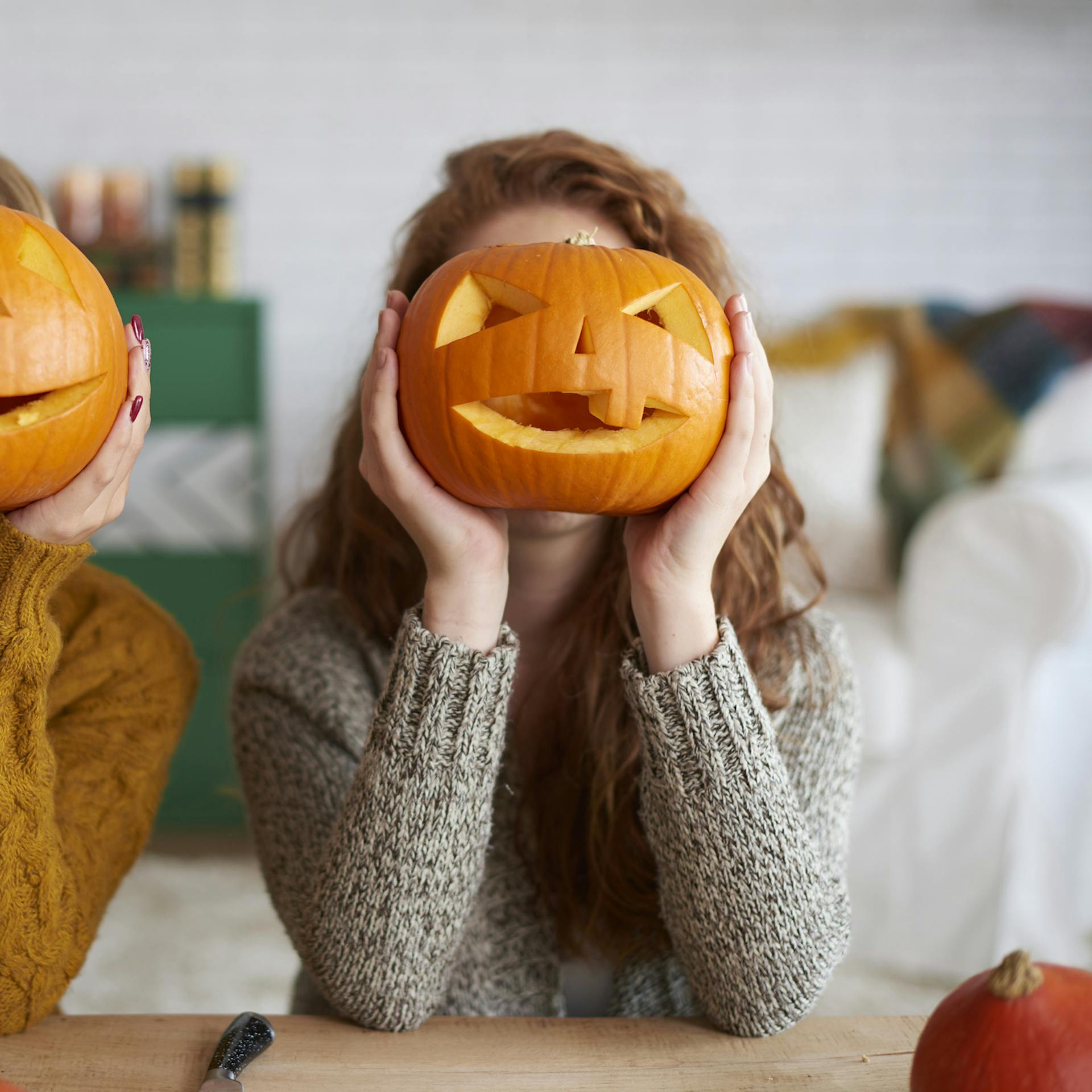 Due donne tengono delle zucche intagliate davanti al volto.
